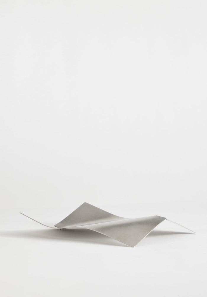 Stainless steel bowl in a wave shape, handcrafted from a single sheet, showcasing a minimalist design by Dutch designer Paul Coenen, on a white background.