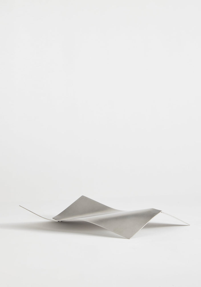 Stainless steel bowl in a wave shape, handcrafted from a single sheet, showcasing a minimalist design by Dutch designer Paul Coenen, on a white background.