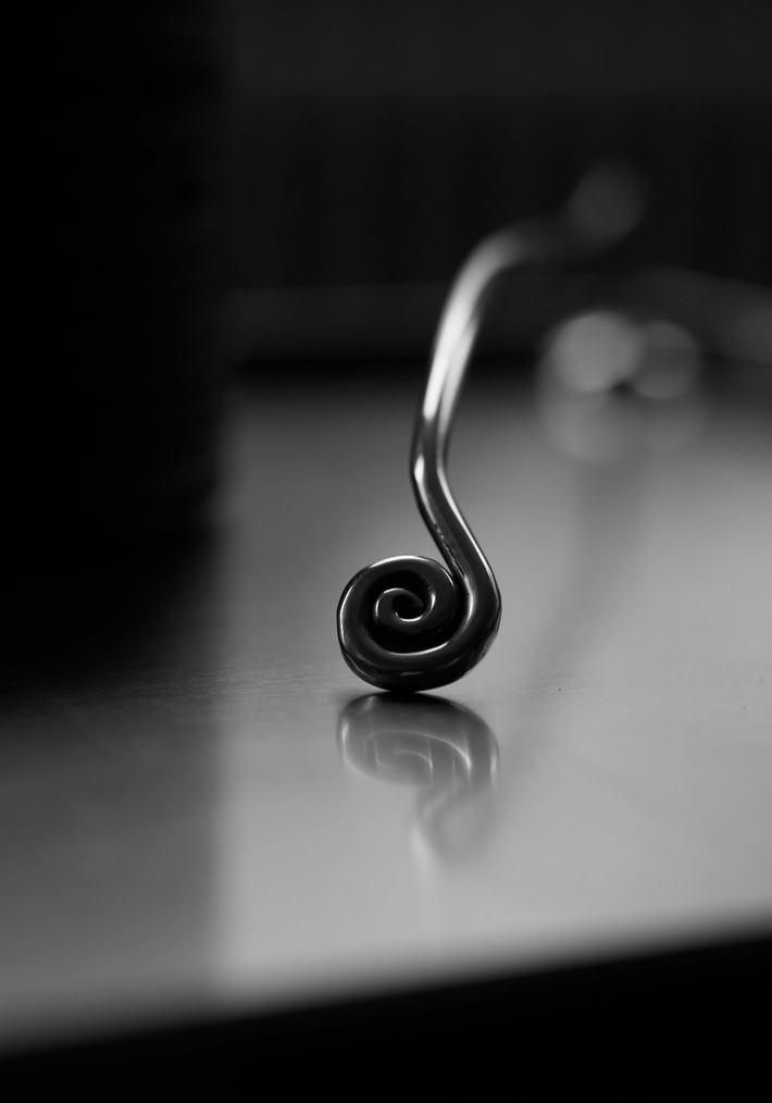 Close-up of Candle Stopper | silver, featuring a spiraled stainless steel handle resting on a reflective surface, highlighting its elegant, organic design for candle extinguishing.