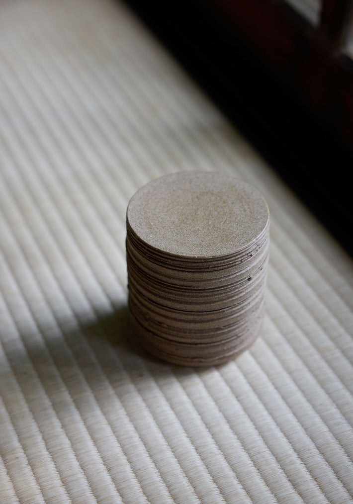 Diplomatico Scented Candle on woven mat, showcasing thin, light-brown pads. Ceramic vessel by Alex Gabriels, designed for reuse, with a woody-aromatic fragrance.