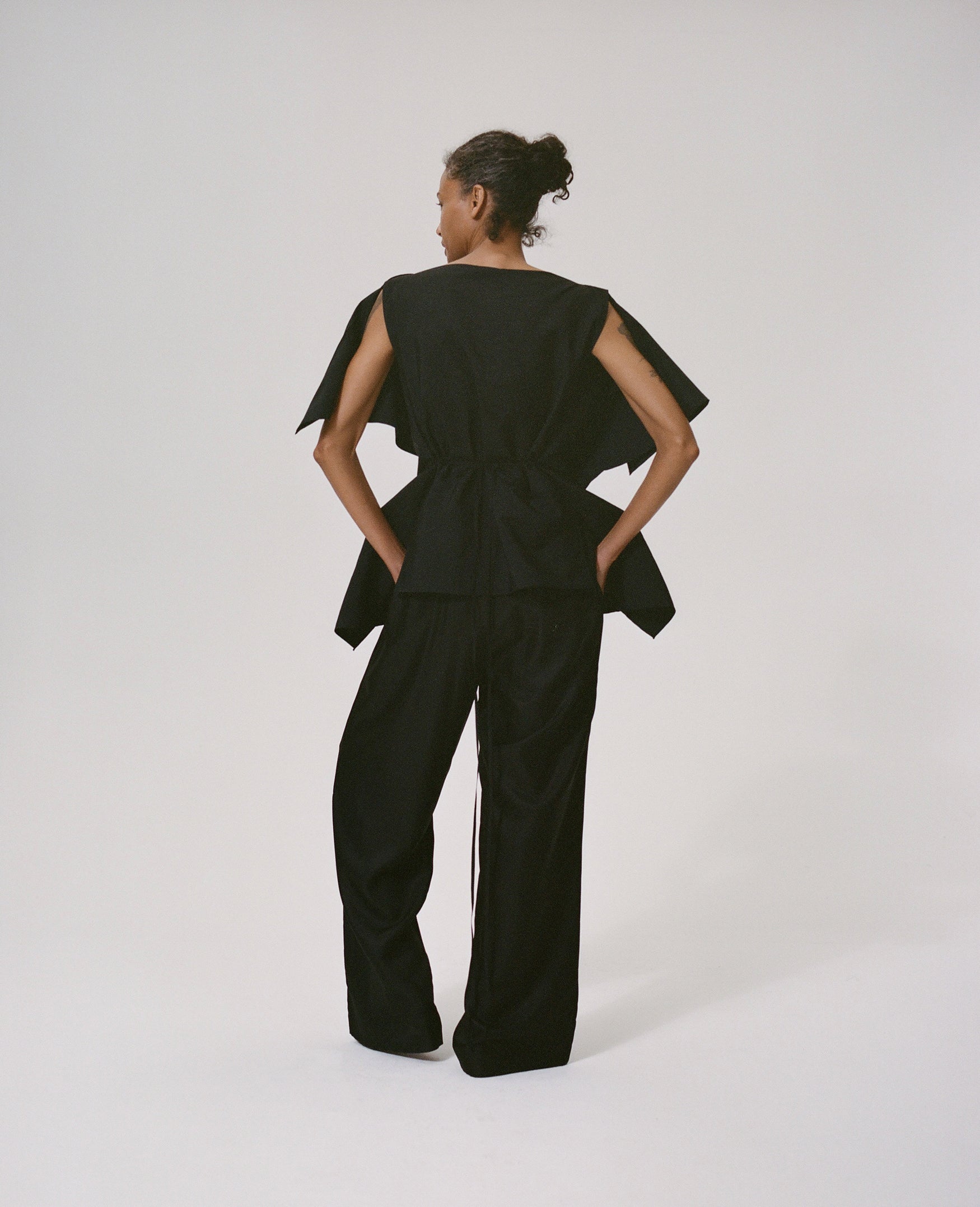 Woman wearing a black origami inspired top with black silk trousers on a white background