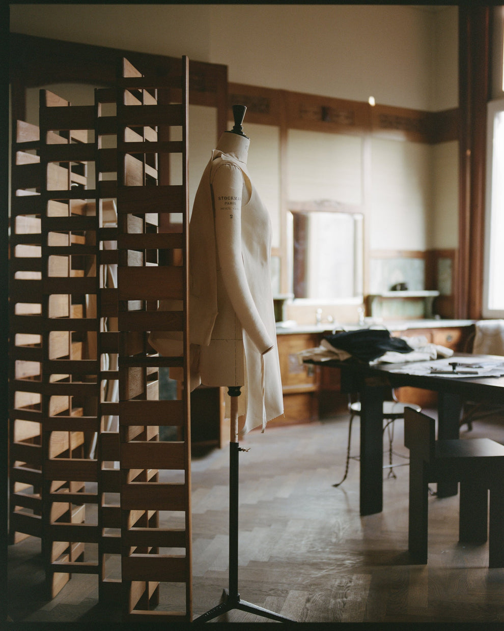Mannequin wearing a canvas toile in a room with a decorative screen and table.