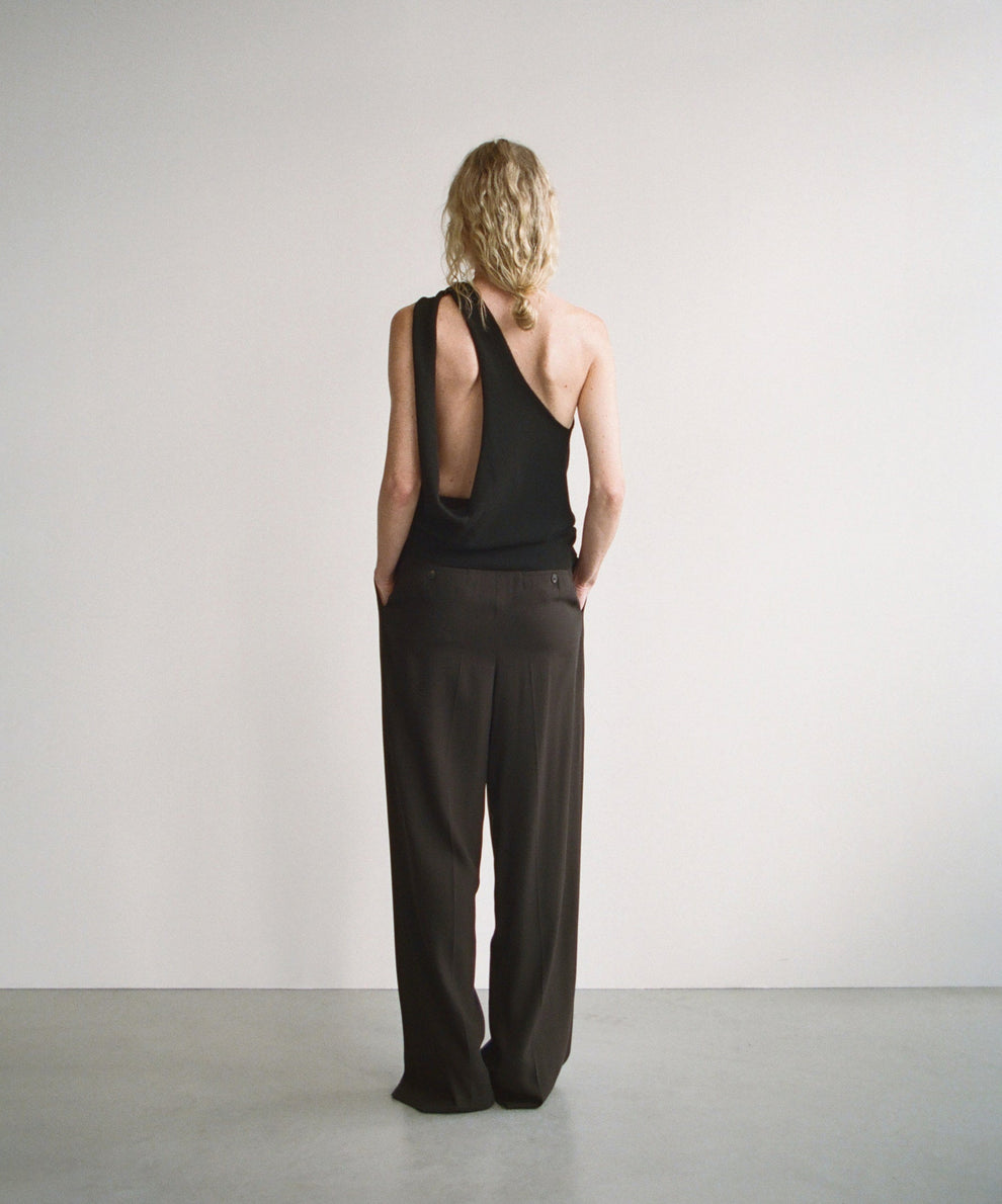 Person wearing a black one shoulder knitted top with open back detail and black wide-leg pants against a plain background