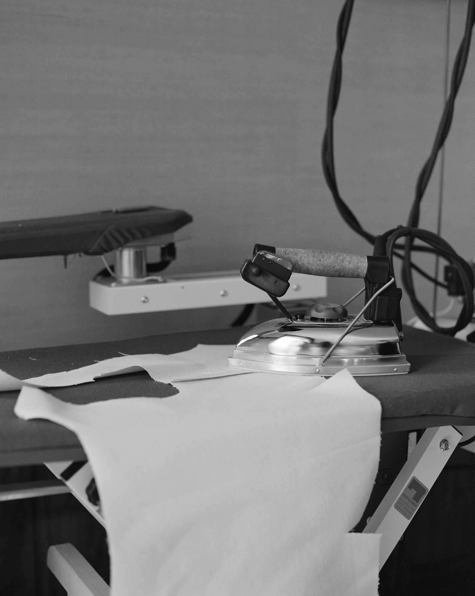 Ironing board with iron and clothes against a linnen covered wall