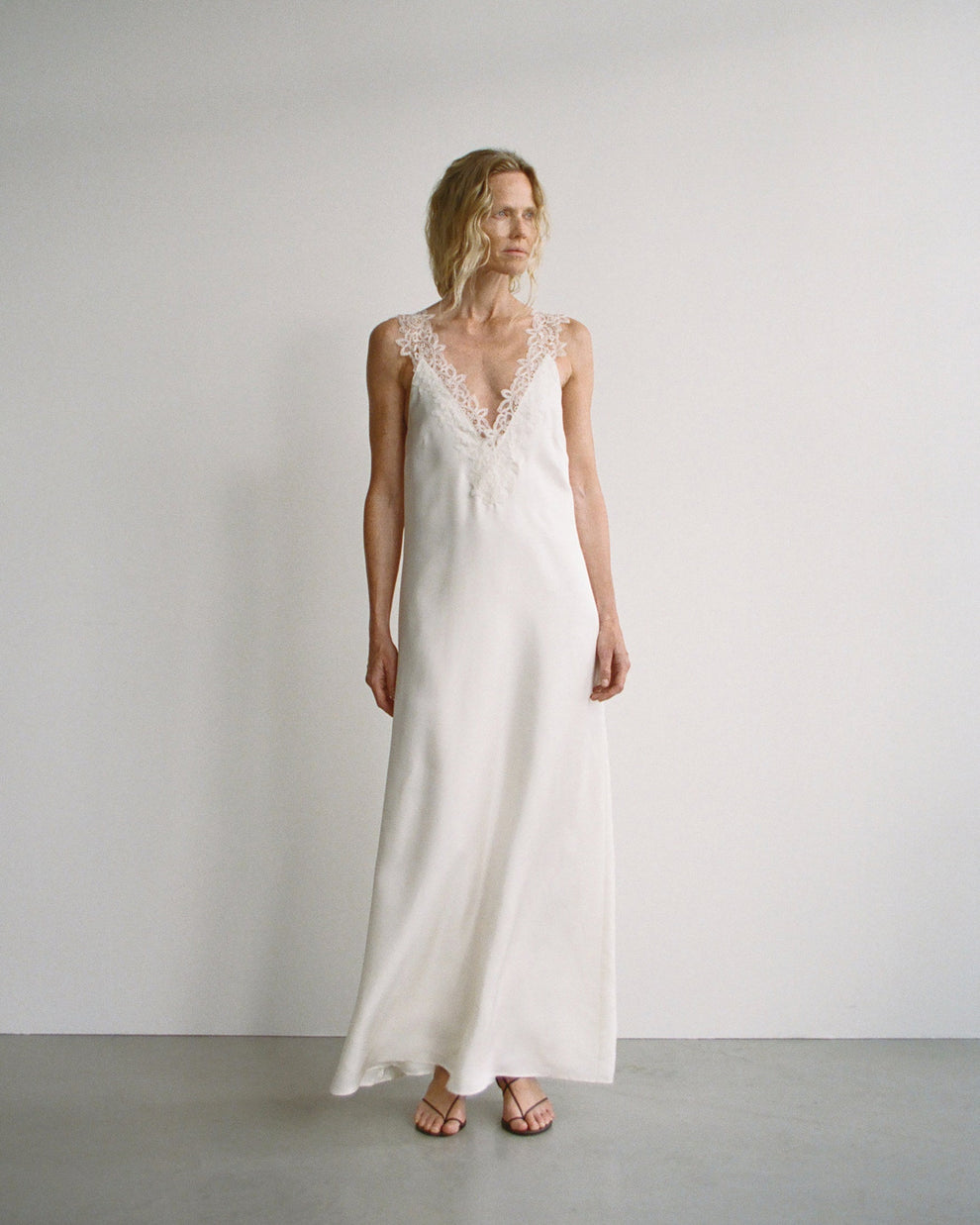 Woman wearing a white slip dress with lace details against a plain background