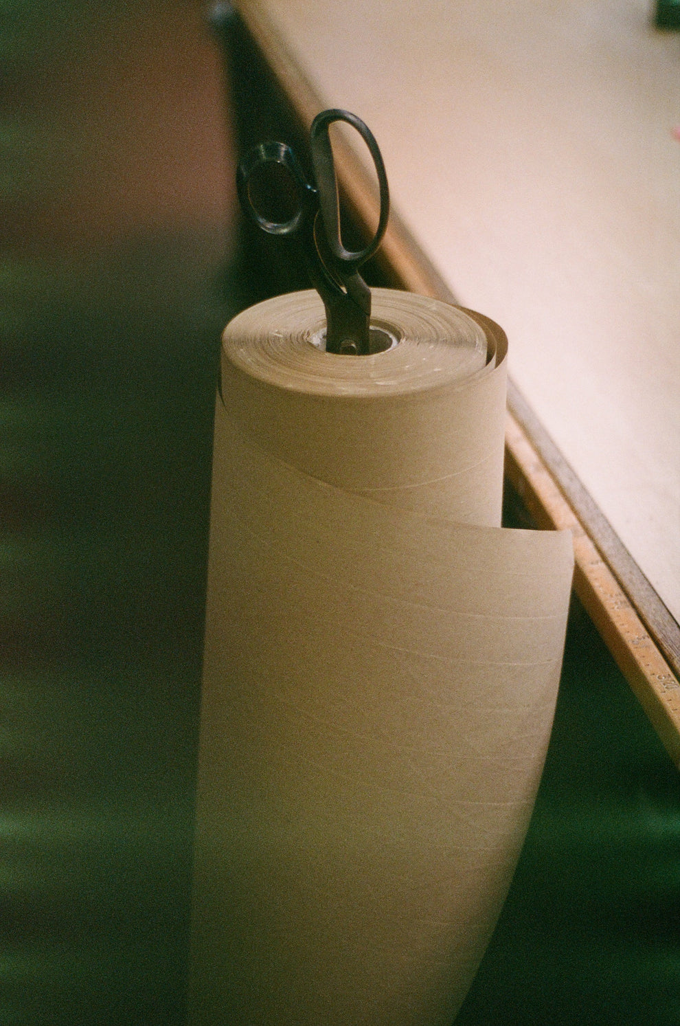 Roll of brown paper with a pair of scissors on top, placed on a wooden surface.