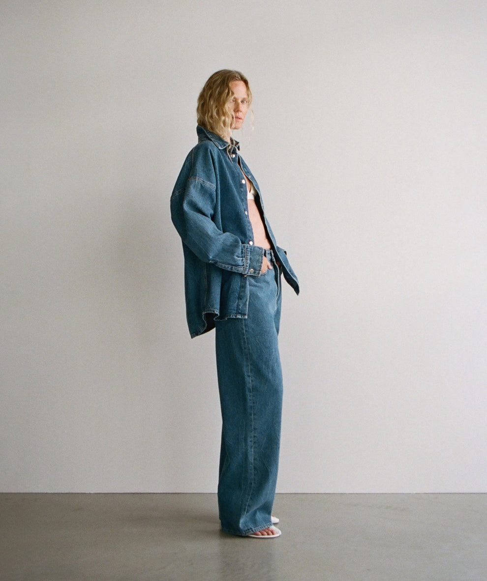 Woman wearing a denim overshirt and matching denim wide leg jeans against a white backdrop