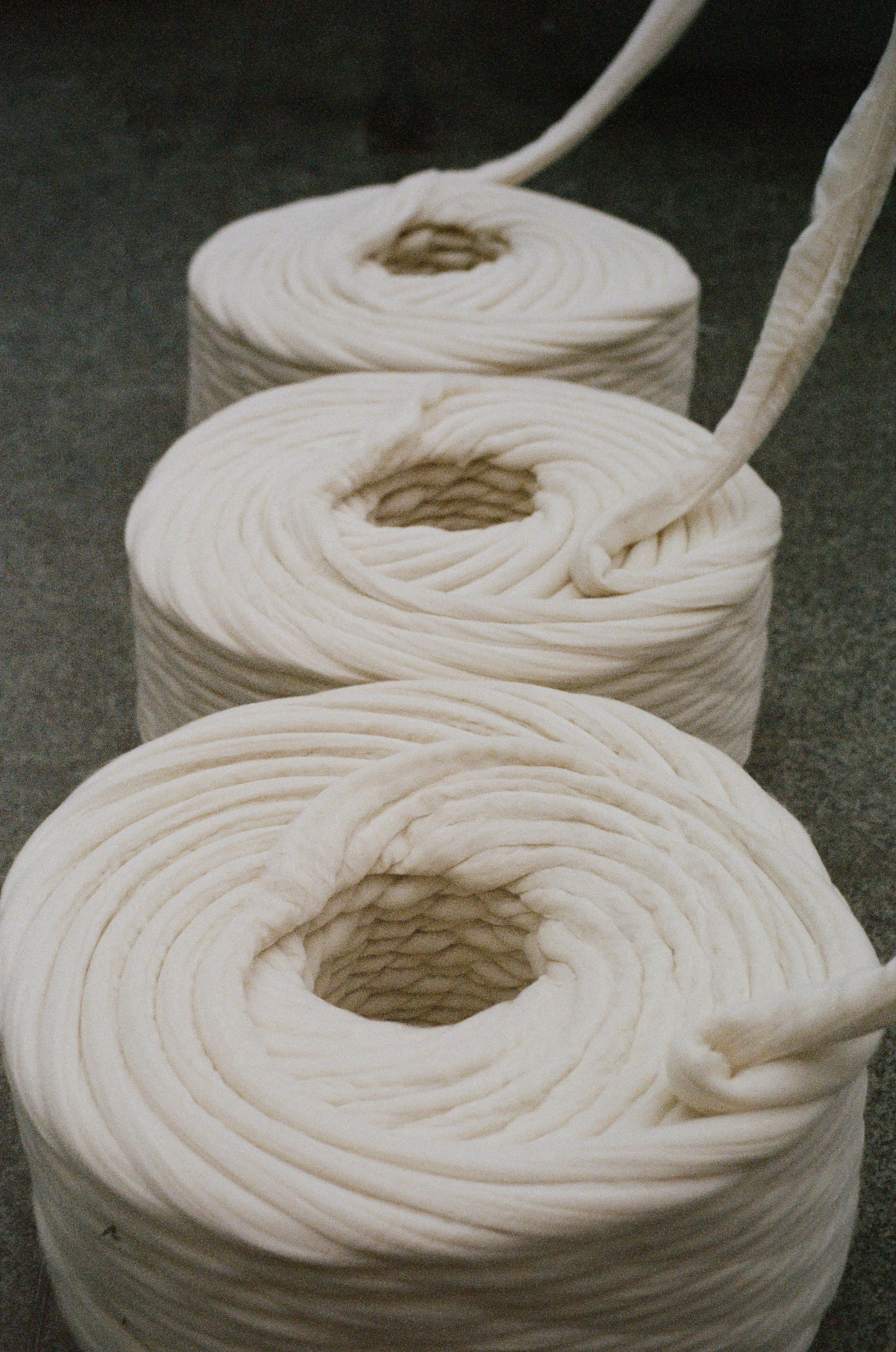 Three rolls of thick cream wool yarn on a dark surface