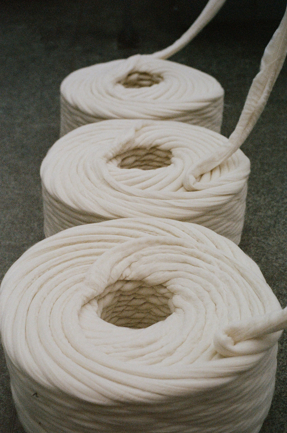 Three rolls of thick cream wool yarn on a dark surface