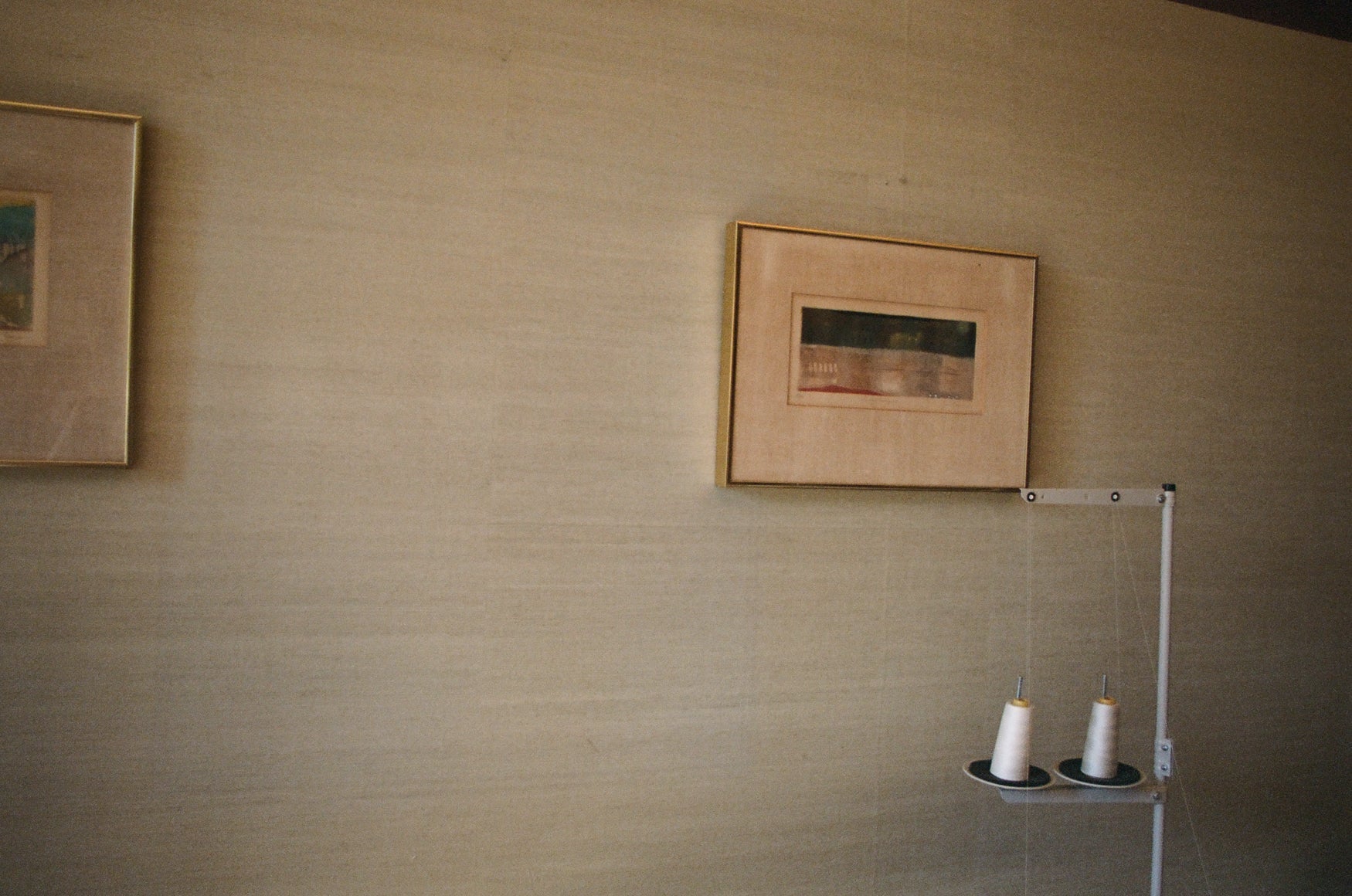 Beige linnen wall with framed artwork and a sewing machine detail of thread 