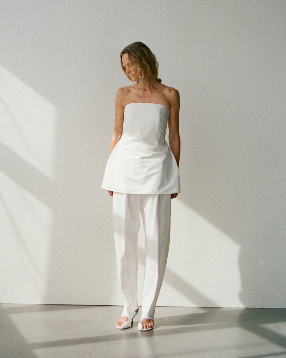 Woman wearing a white strapless cotton poplin top and matching pants against a light background