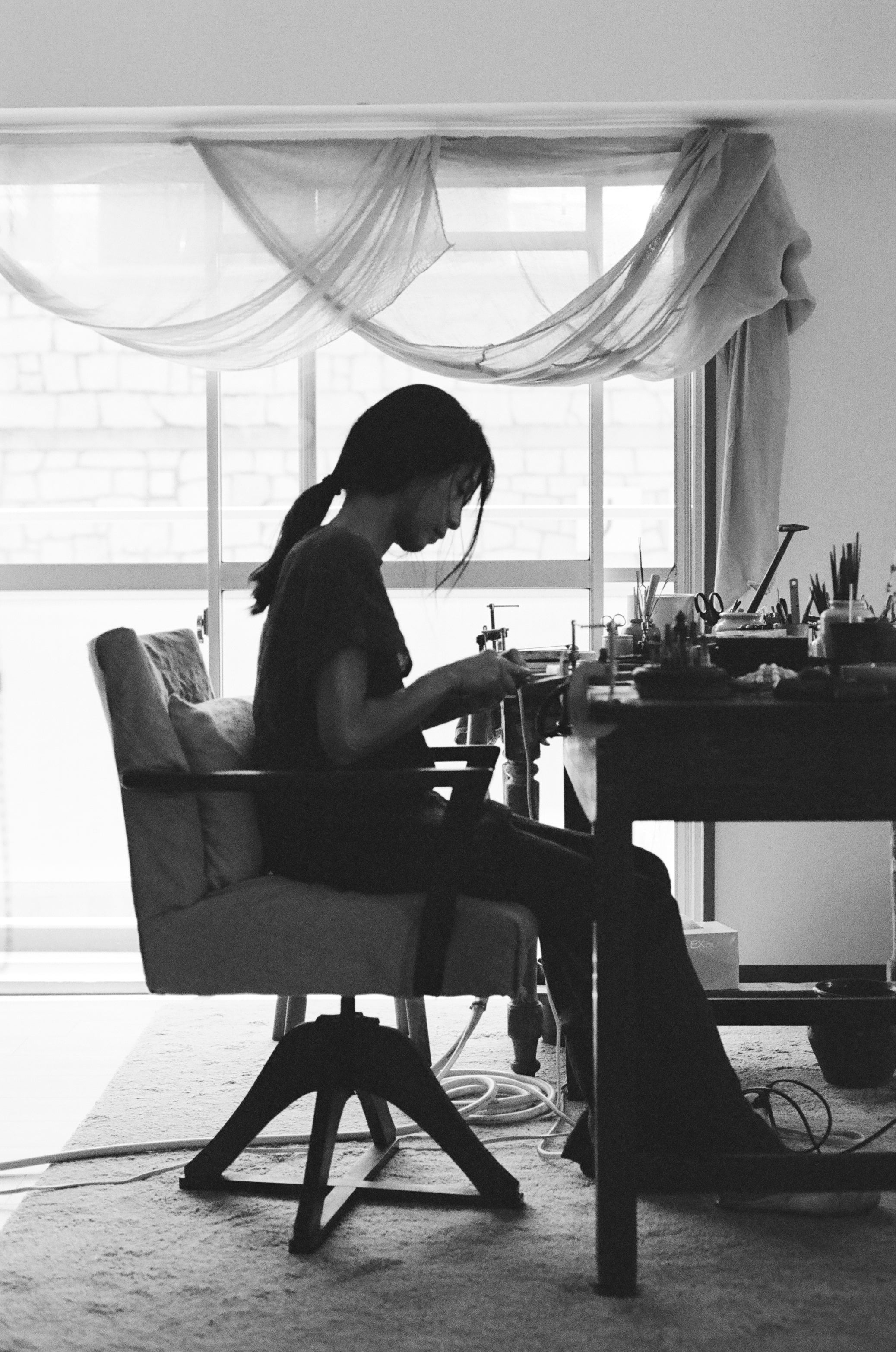 Black and white image of a woman working behind a table with different kinds of small tools 