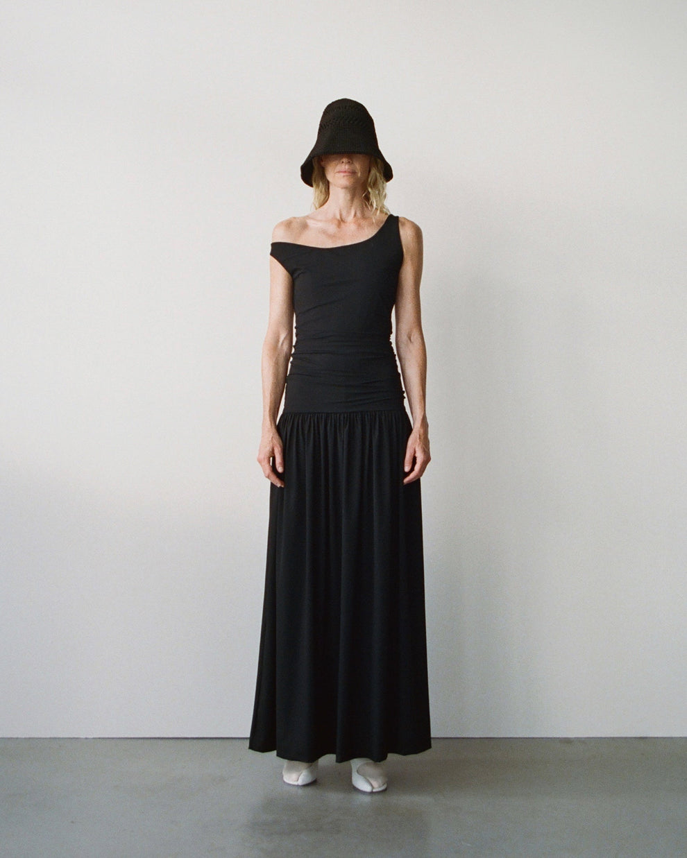 Person wearing a black off-shoulder dress and black straw hat against a white background