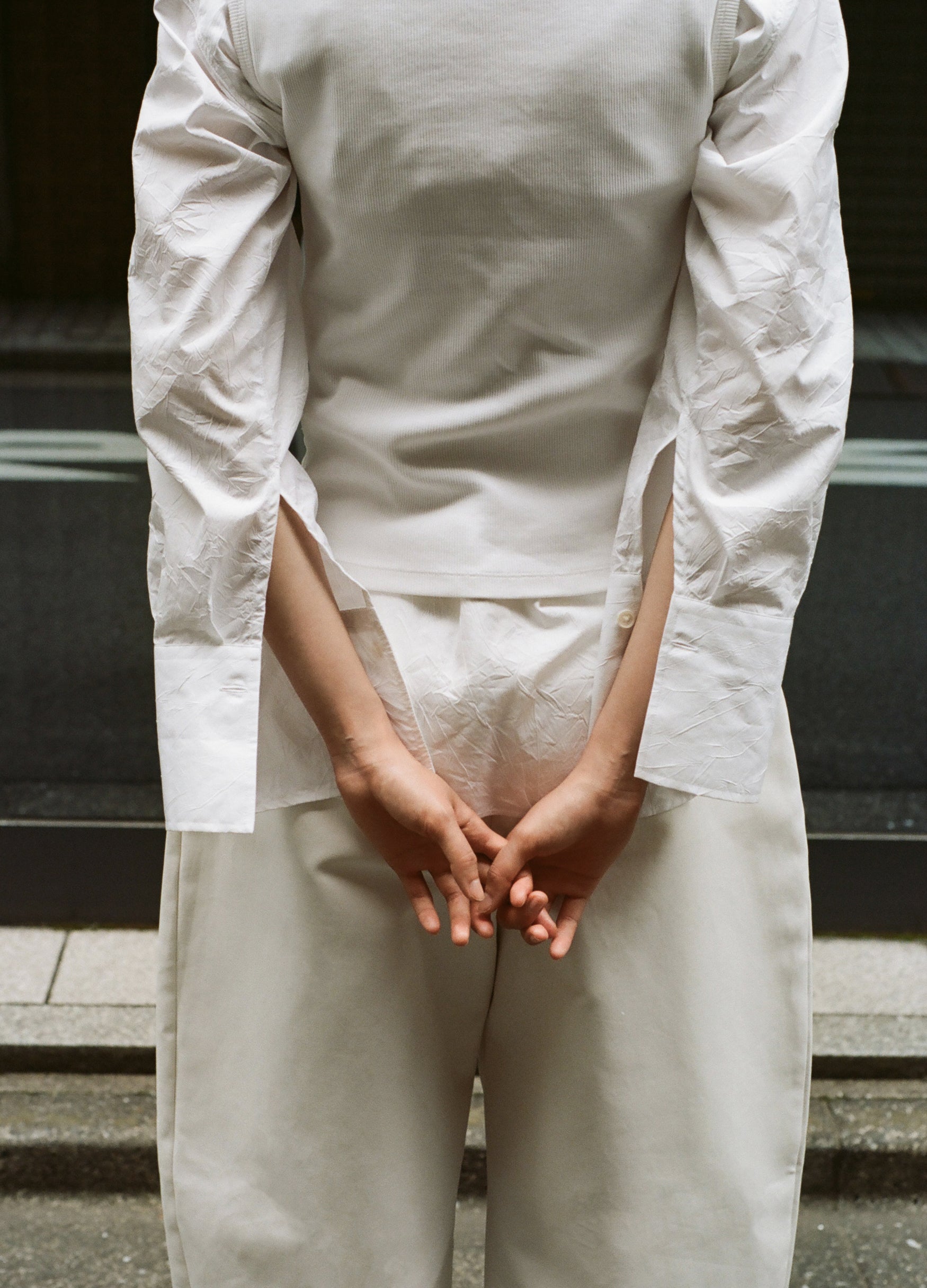 Person photographed from the back, wearing a white shirt and sculptural cream trousers. 