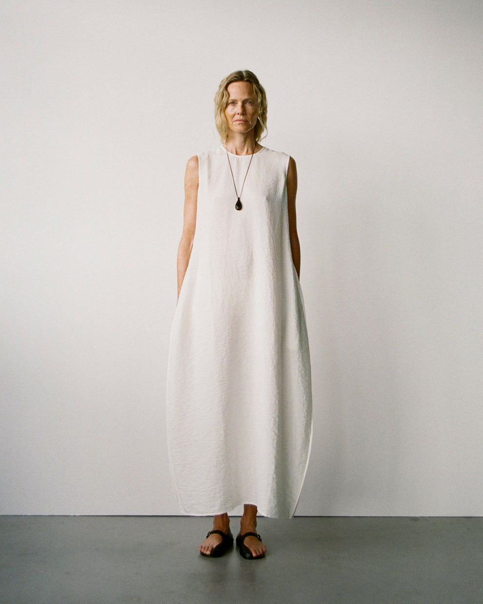 Woman wearing a white sleeveless hammered cupro dress with balloon shape against a plain background