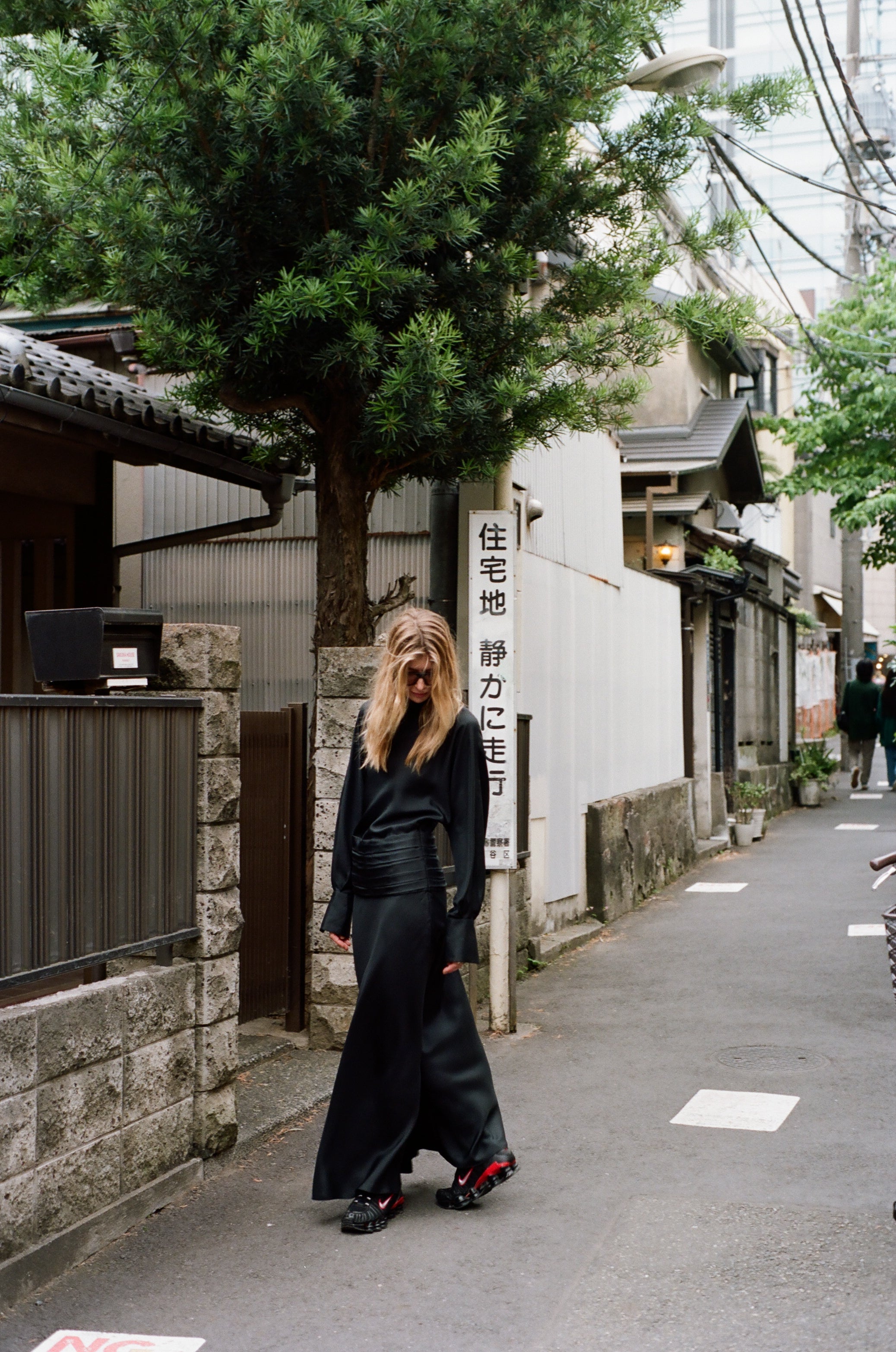 Woman wearing a long black silk dress with nike sneakers in a narrow Tokyo street