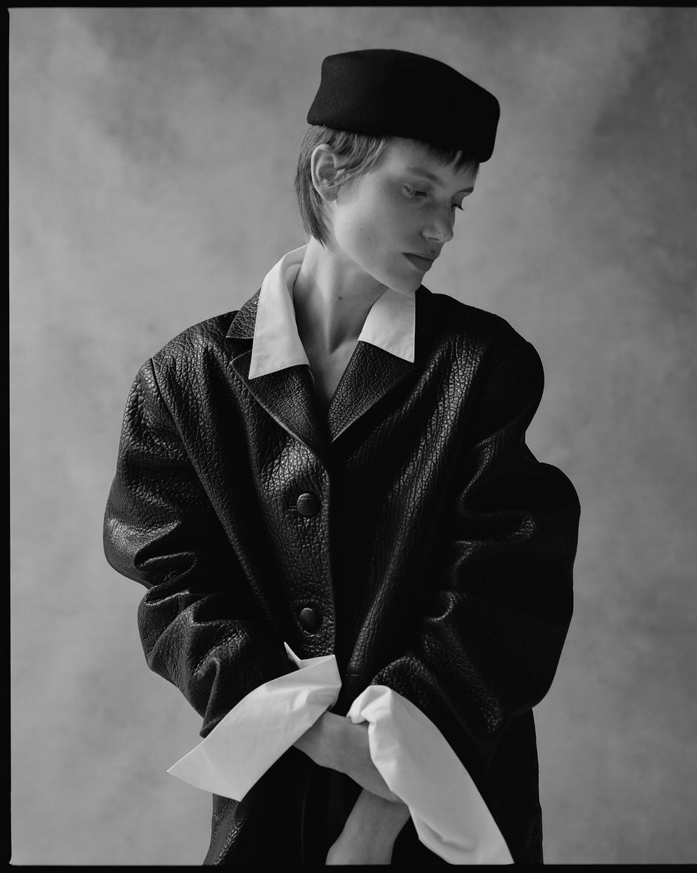 Portrait of a woman wearing a black pill box hat and a textured black leather blazer