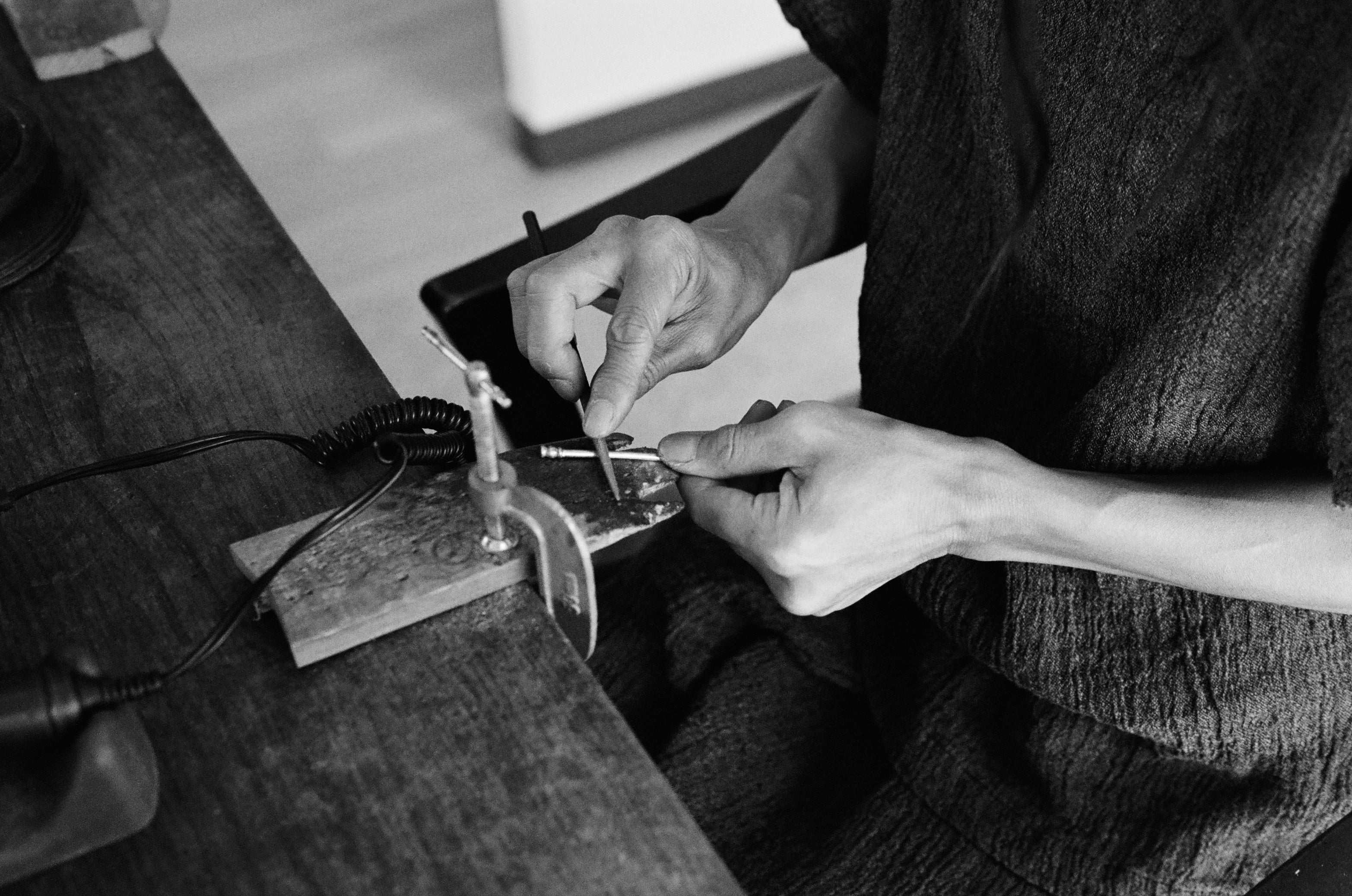Black and white image of a woman working behind a table with different kinds of small tools 