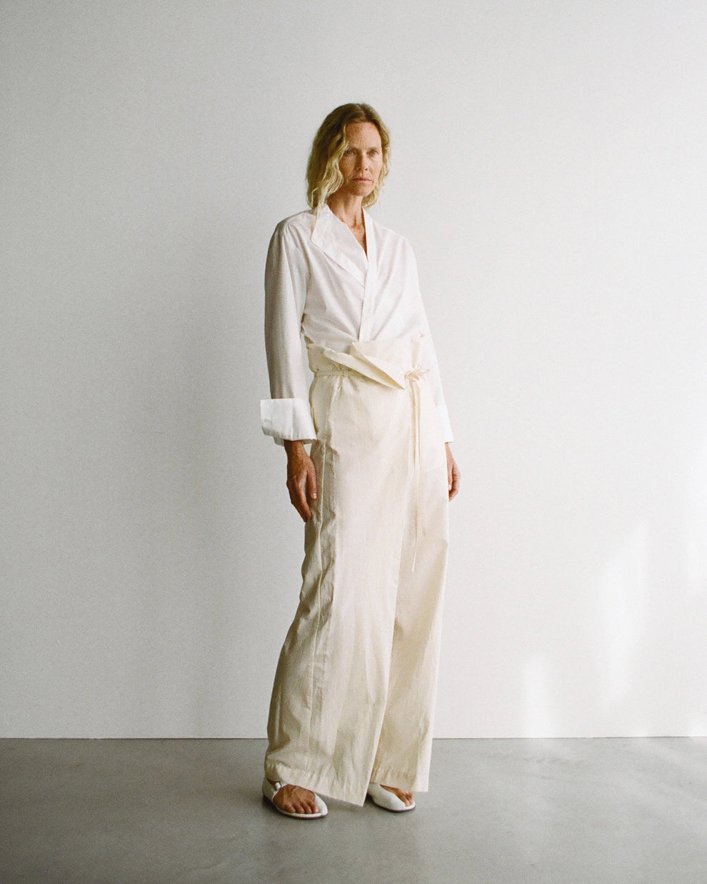 Woman wearing a white wrap shirt with beige cotton wide leg trousers against a plain background