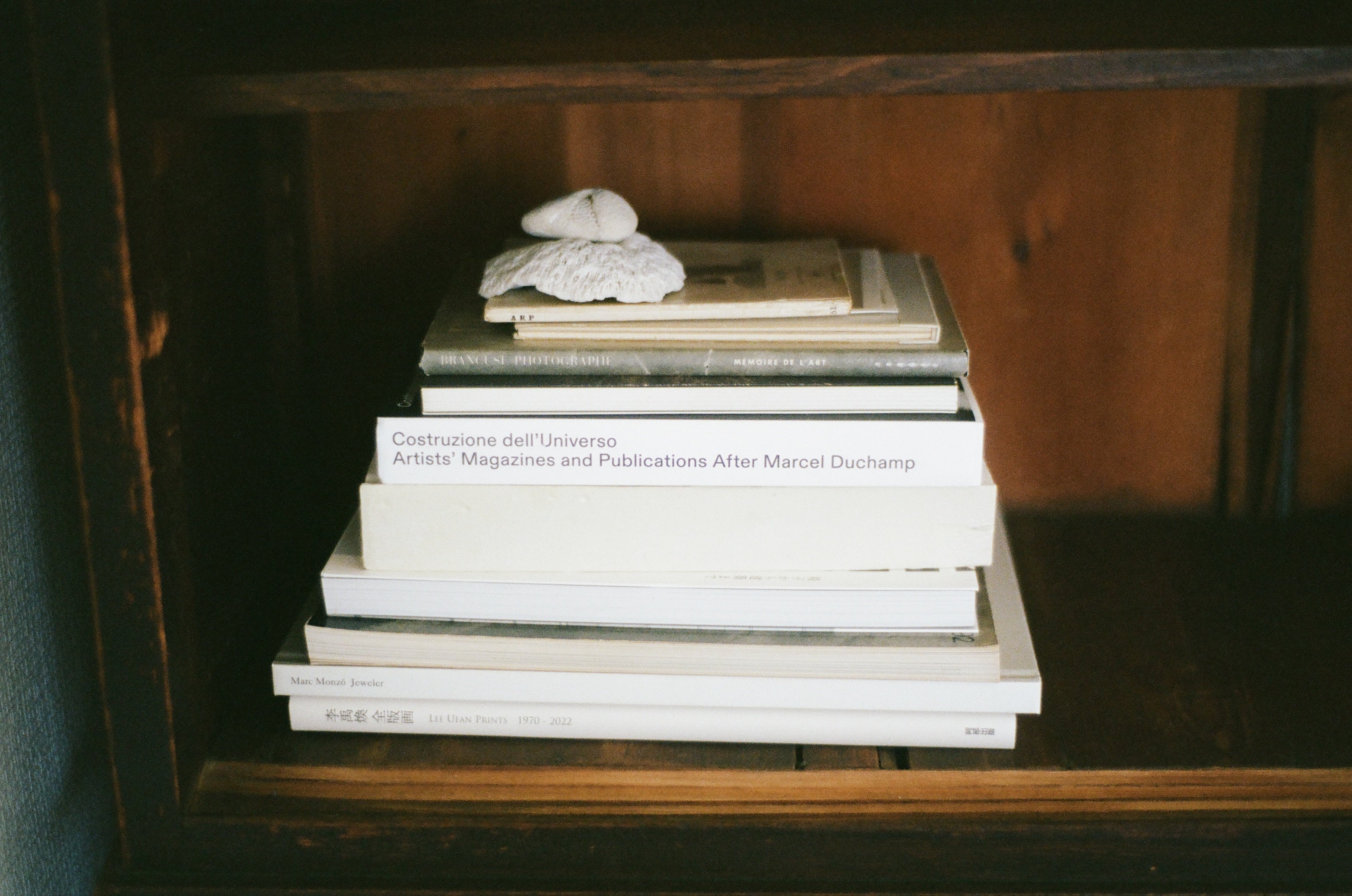 Bookshelf with a stack of art books and a small shell on top