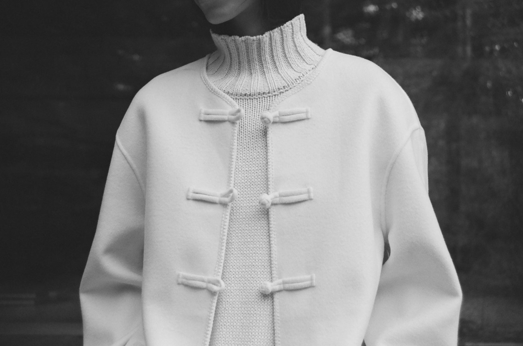 Close-up image of a cream turtleneck and a jacket with mandarin button details on a dark background