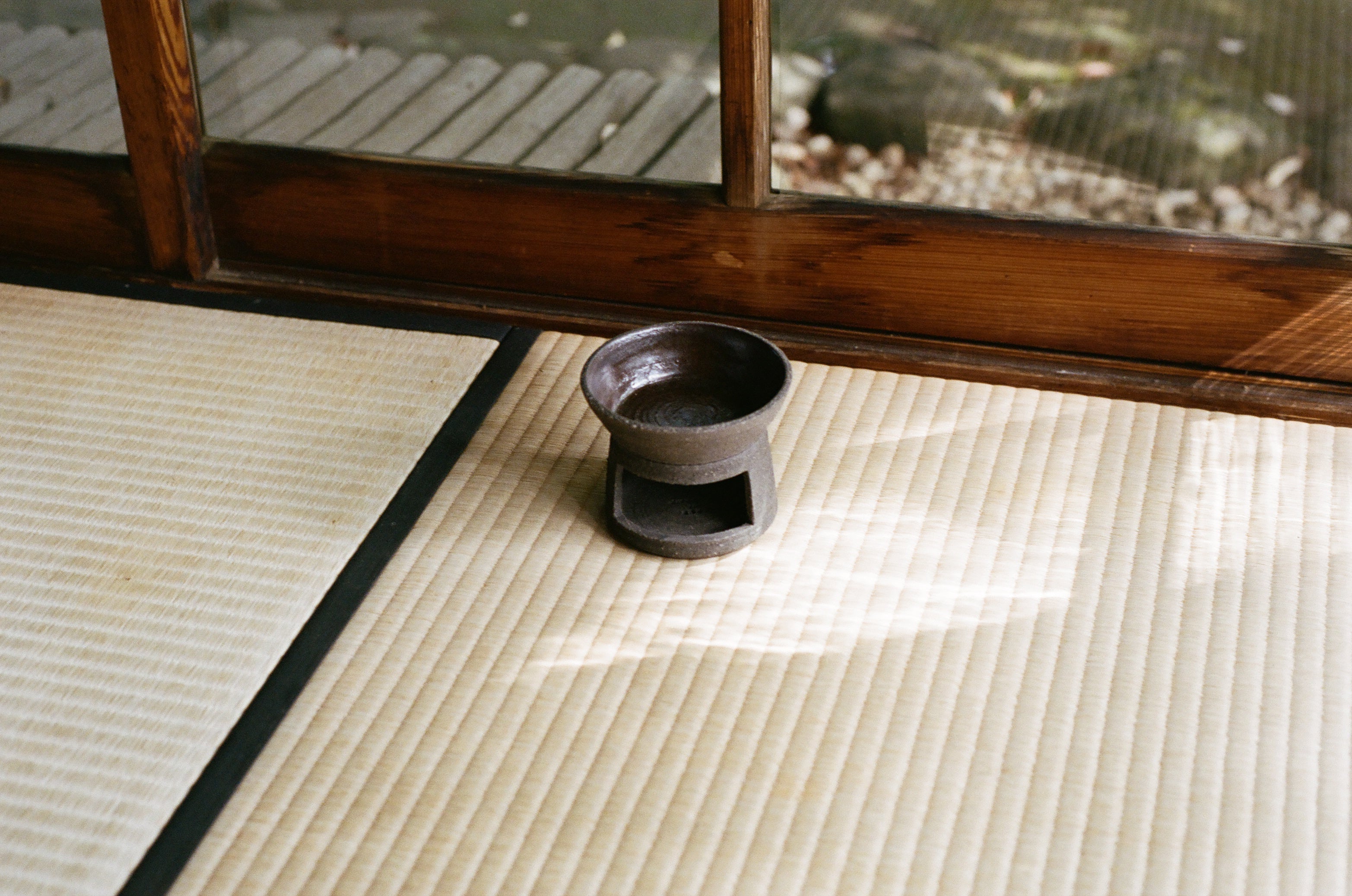 Ceramic oil burner in dark brown clay placed on a tatami mat with wooden window frame