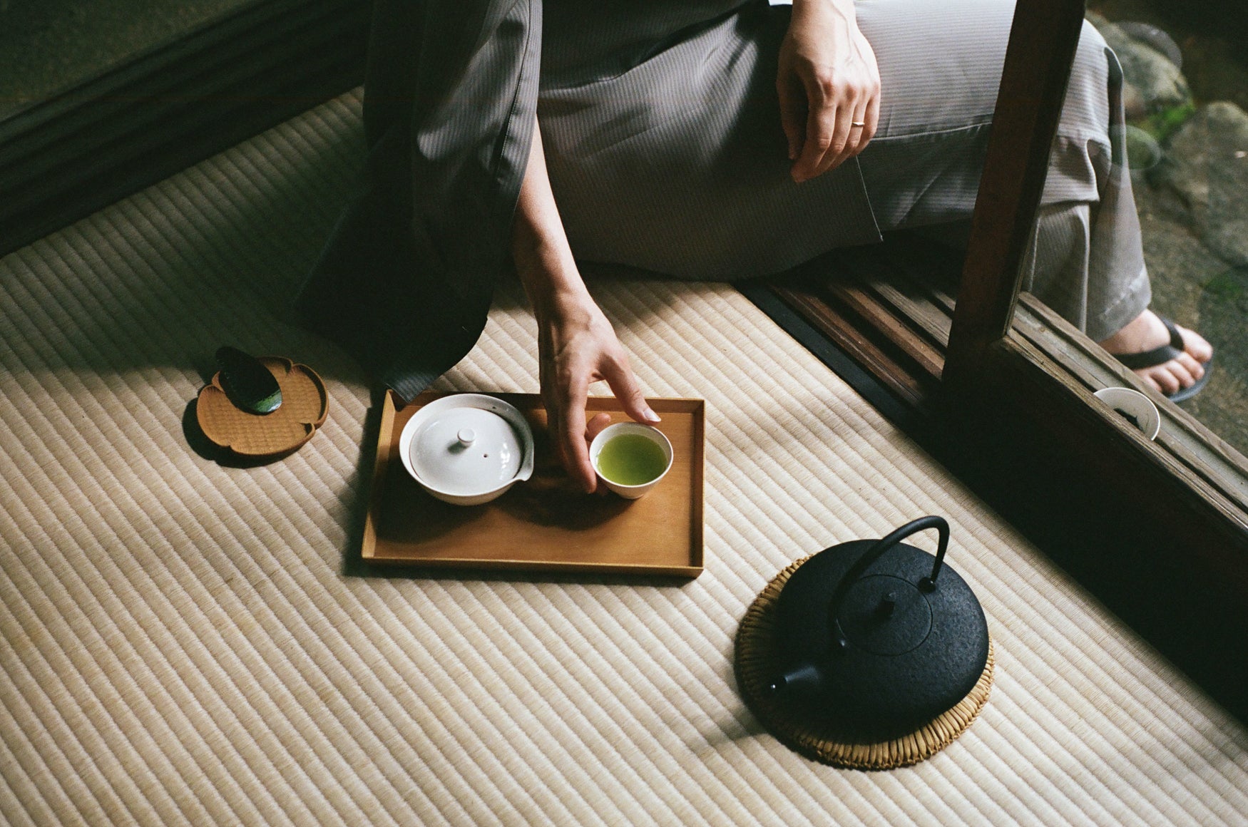 Hand of a woman grabbing a small cup of green tea on a tray on top of a tatami mat. 