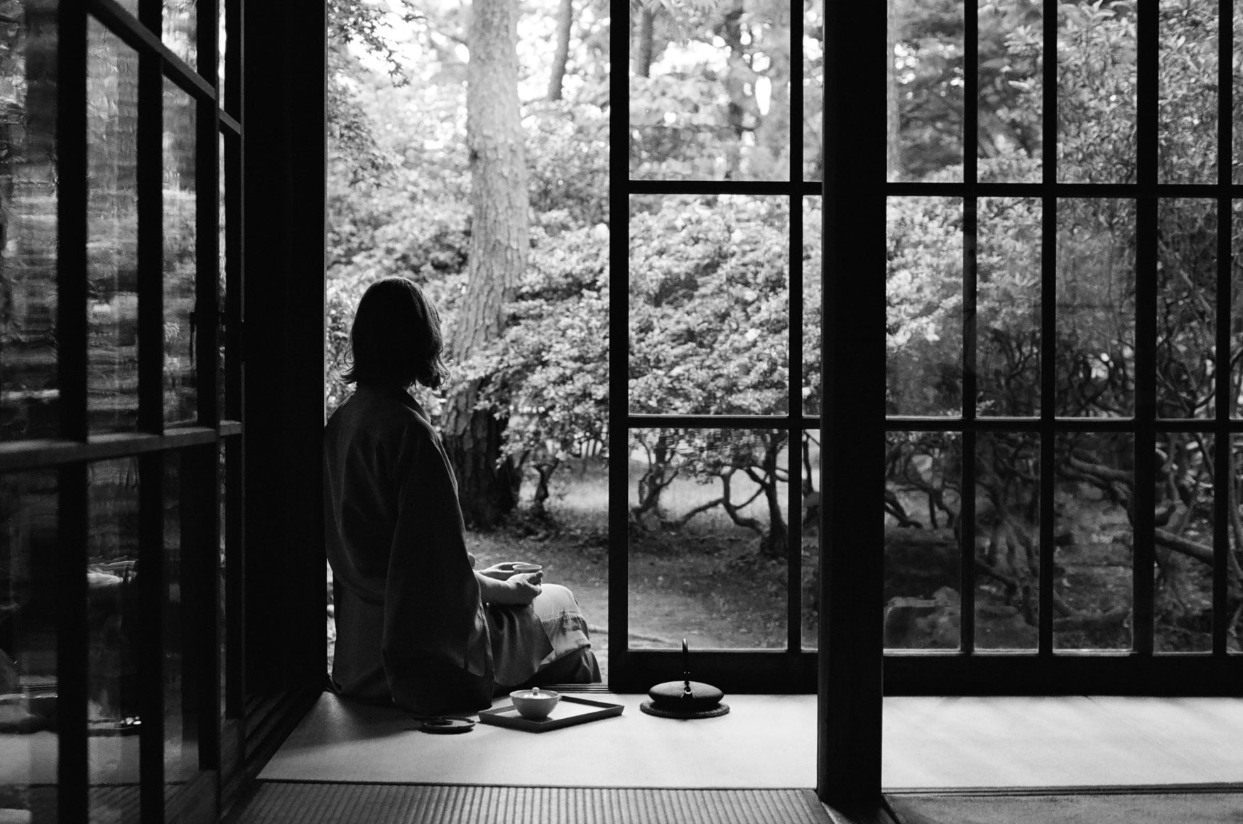 Woman sitting on the edge of a Japanese tea house with the window doors open. 