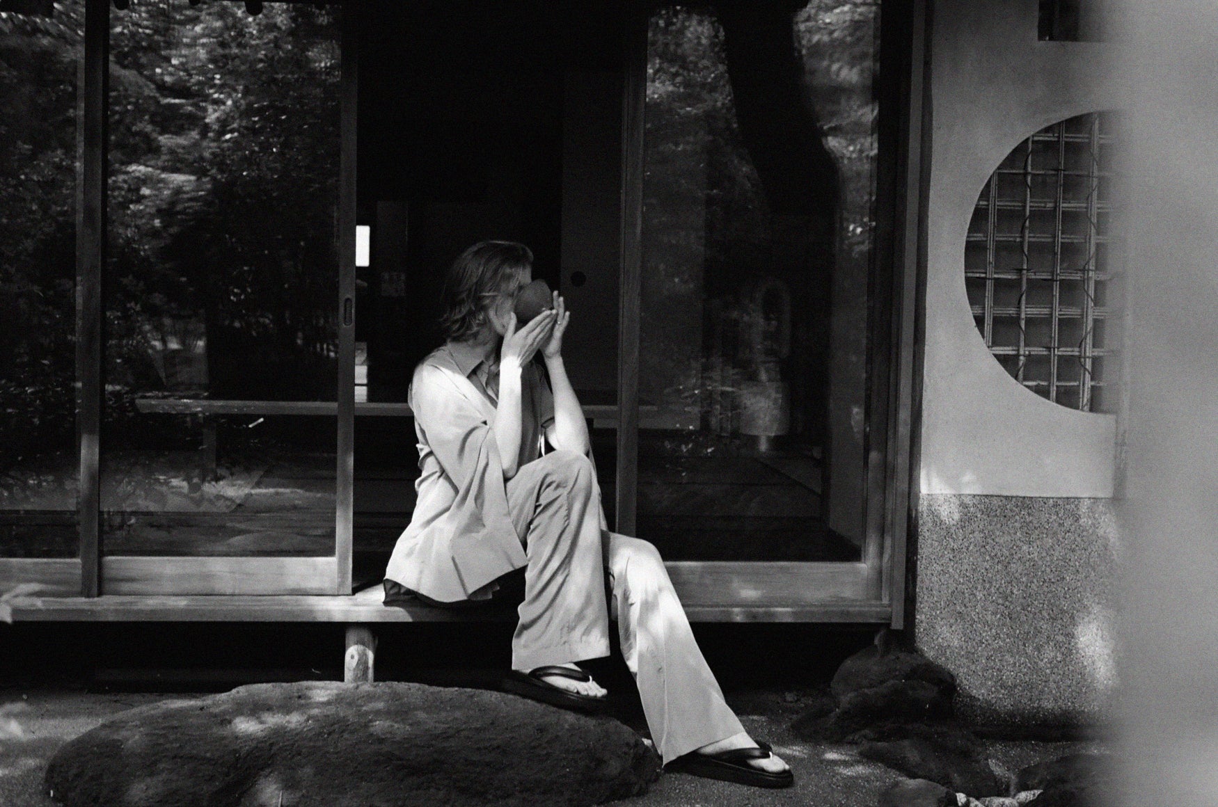 Woman sitting on the edge of a tea house between to glass doors drinking tea. 