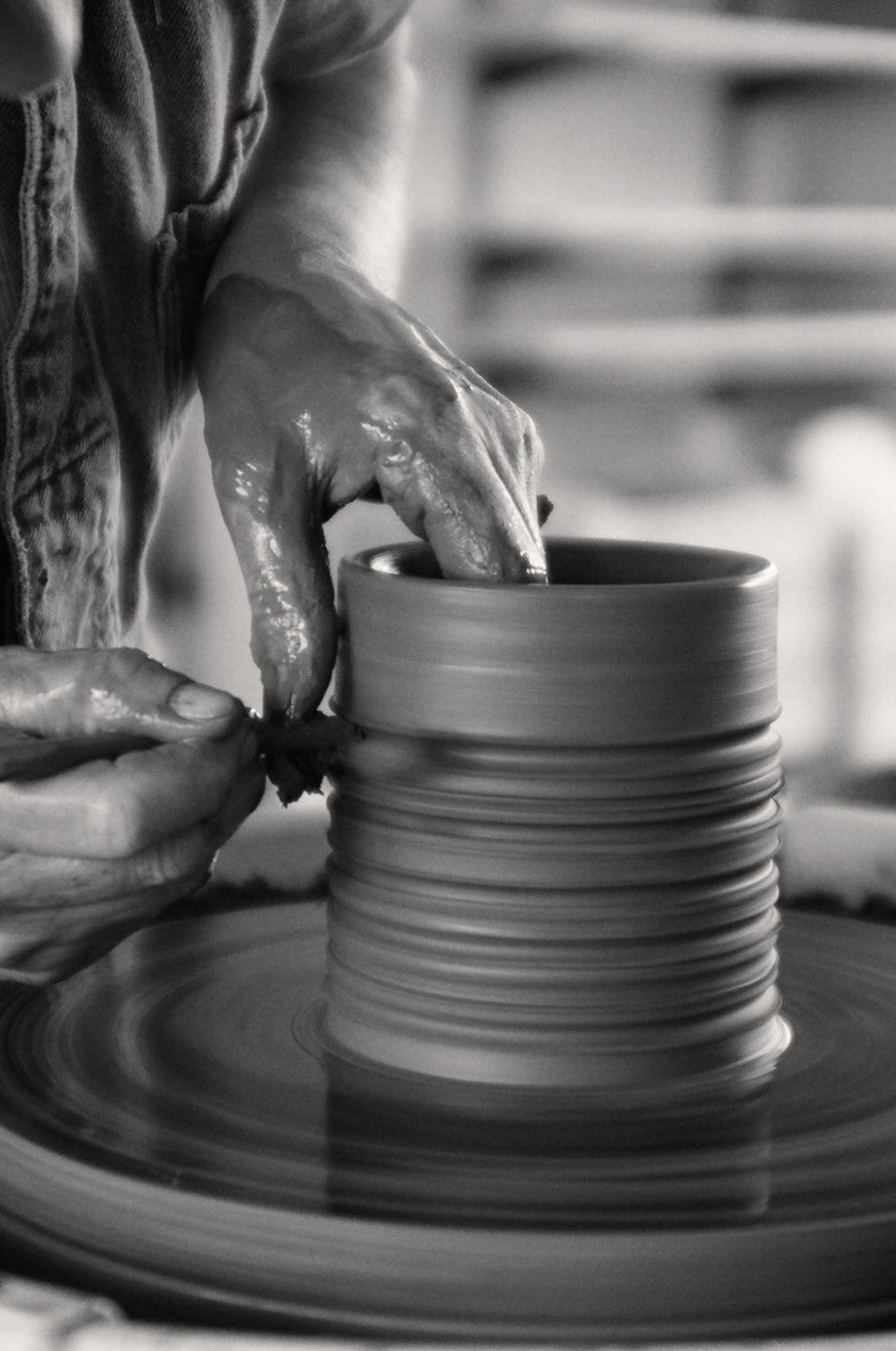 Person working on a clay pot, carving it with a stick on a pottery wheel