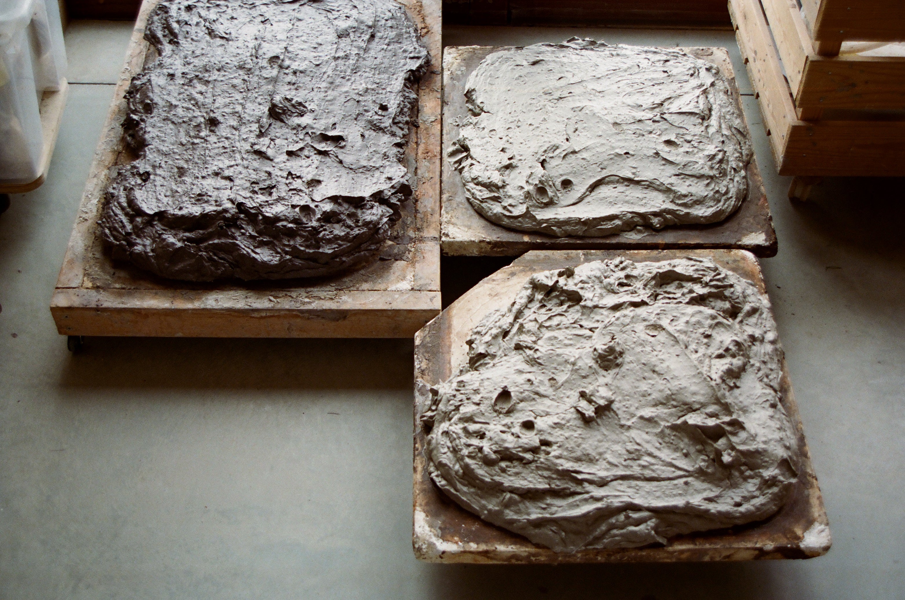 Three rectangular slabs of clay drying on wooden stands on a concrete floor.
