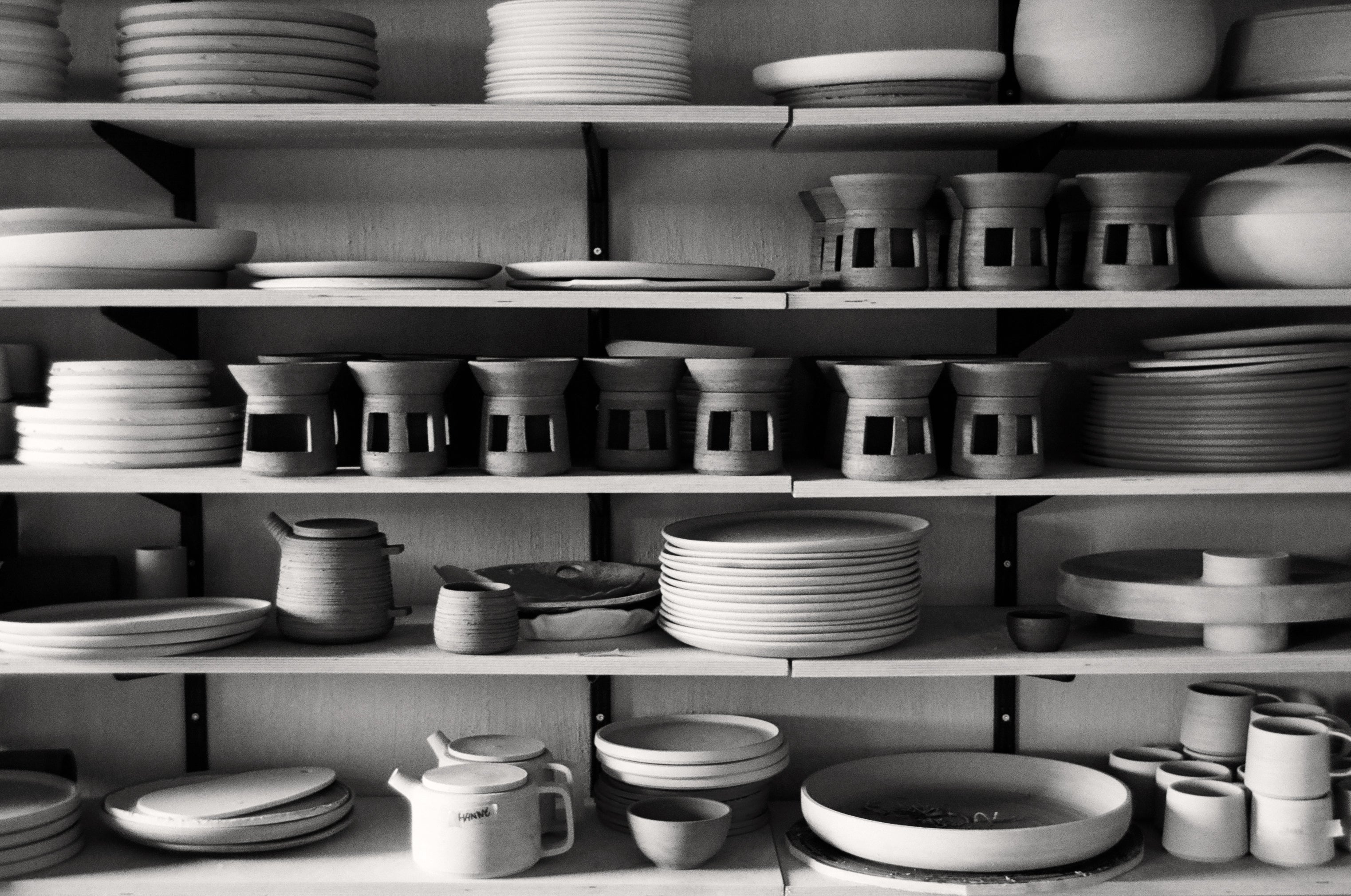 Shelves filled with various ceramic dishes and pots in a black and white photo.