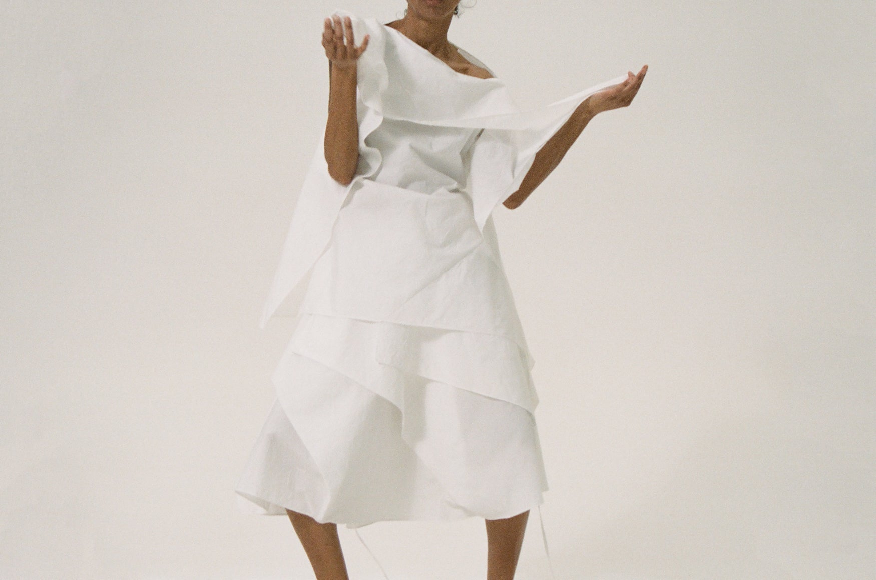 Woman wearing a white origami inspired top and skirt with folds and layers on a plain background