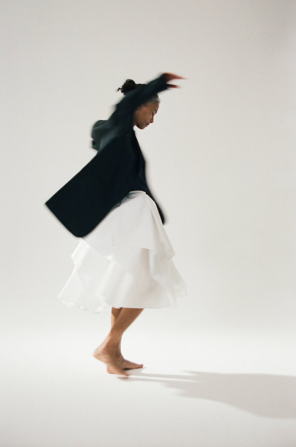 Woman in movement wearing a black blazer and white skirt dancing on a plain background