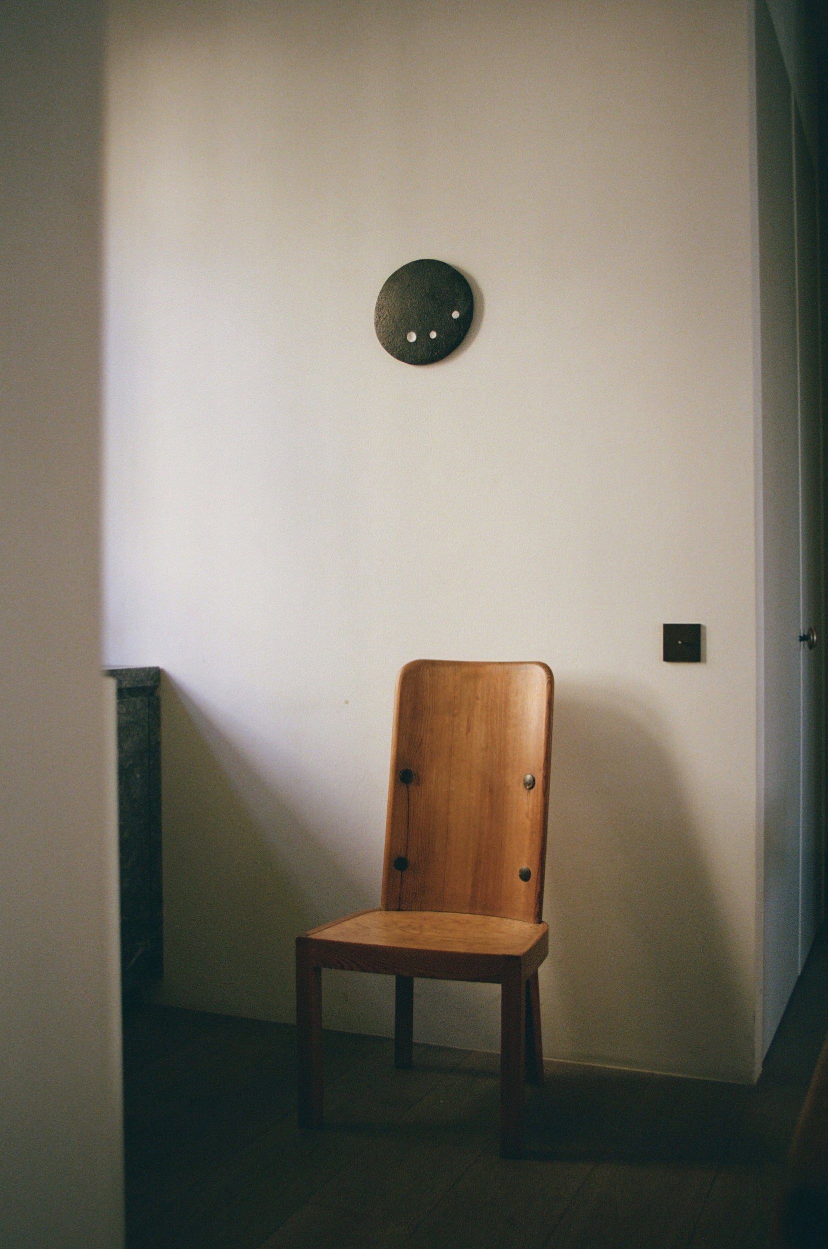 Wooden chair against a plain wall with a stone decorative pieces hanging on the wall