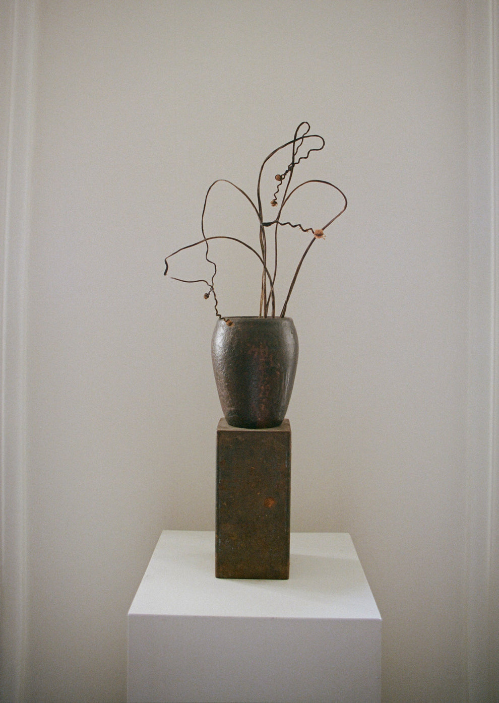 Decorative vase with dried branches on a white pedestal against a plain wall