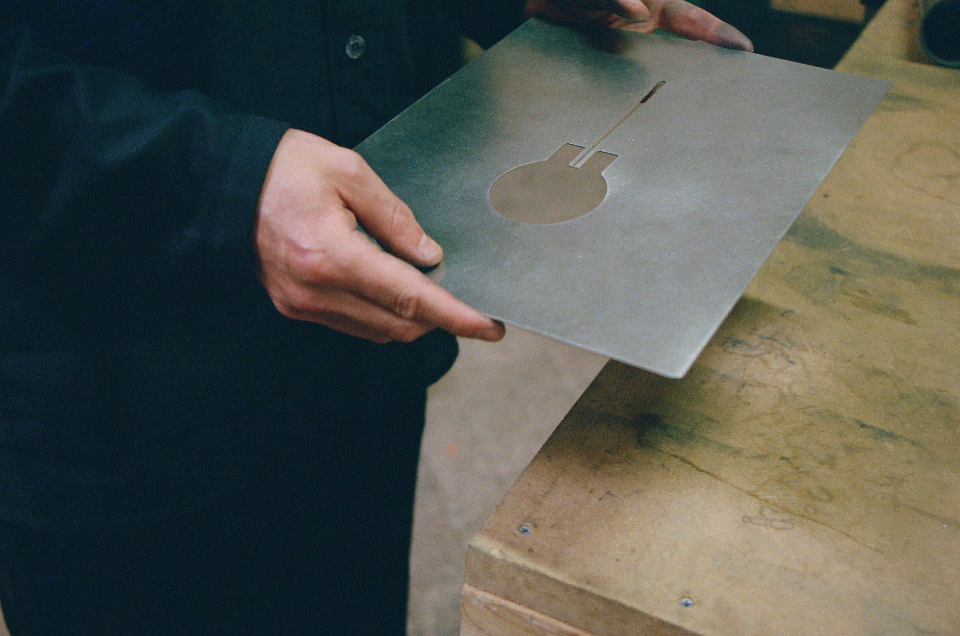 Person holding a stainless steel sheet with a cut-out design on a wooden surface