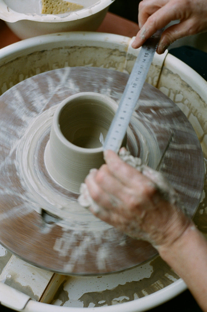 Person measuring a ceramic pot on a wheel