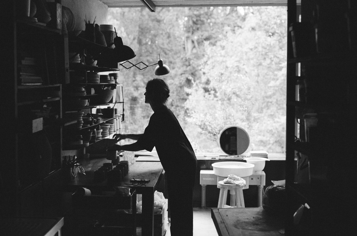 Person working in a ceramic atelier with shelves and a window in the background