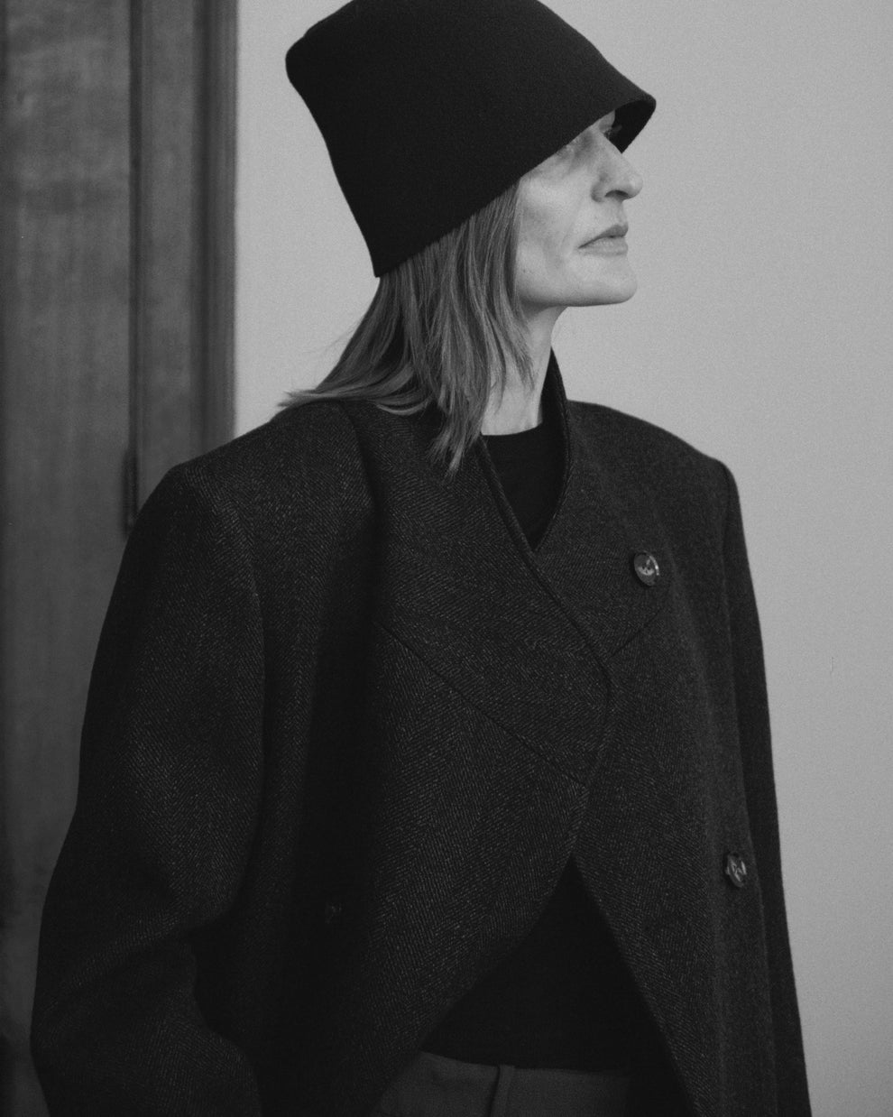 Woman wearing a dark coat and hat against a plain background