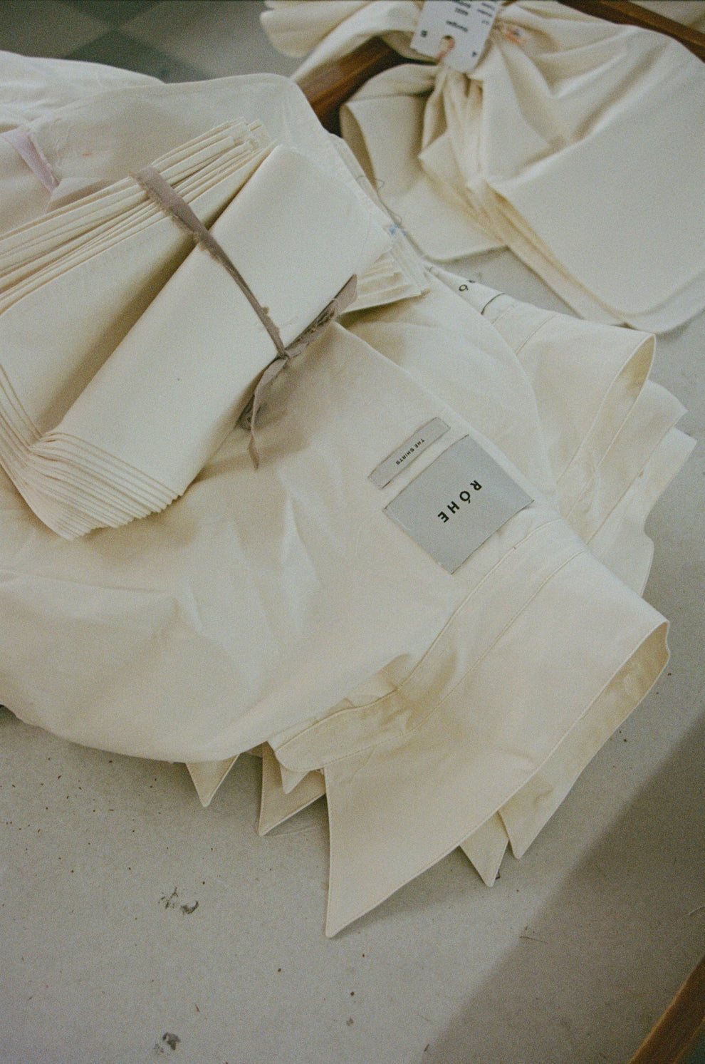 White shirts folded and stacked with a "Róhe" logo label sewn in