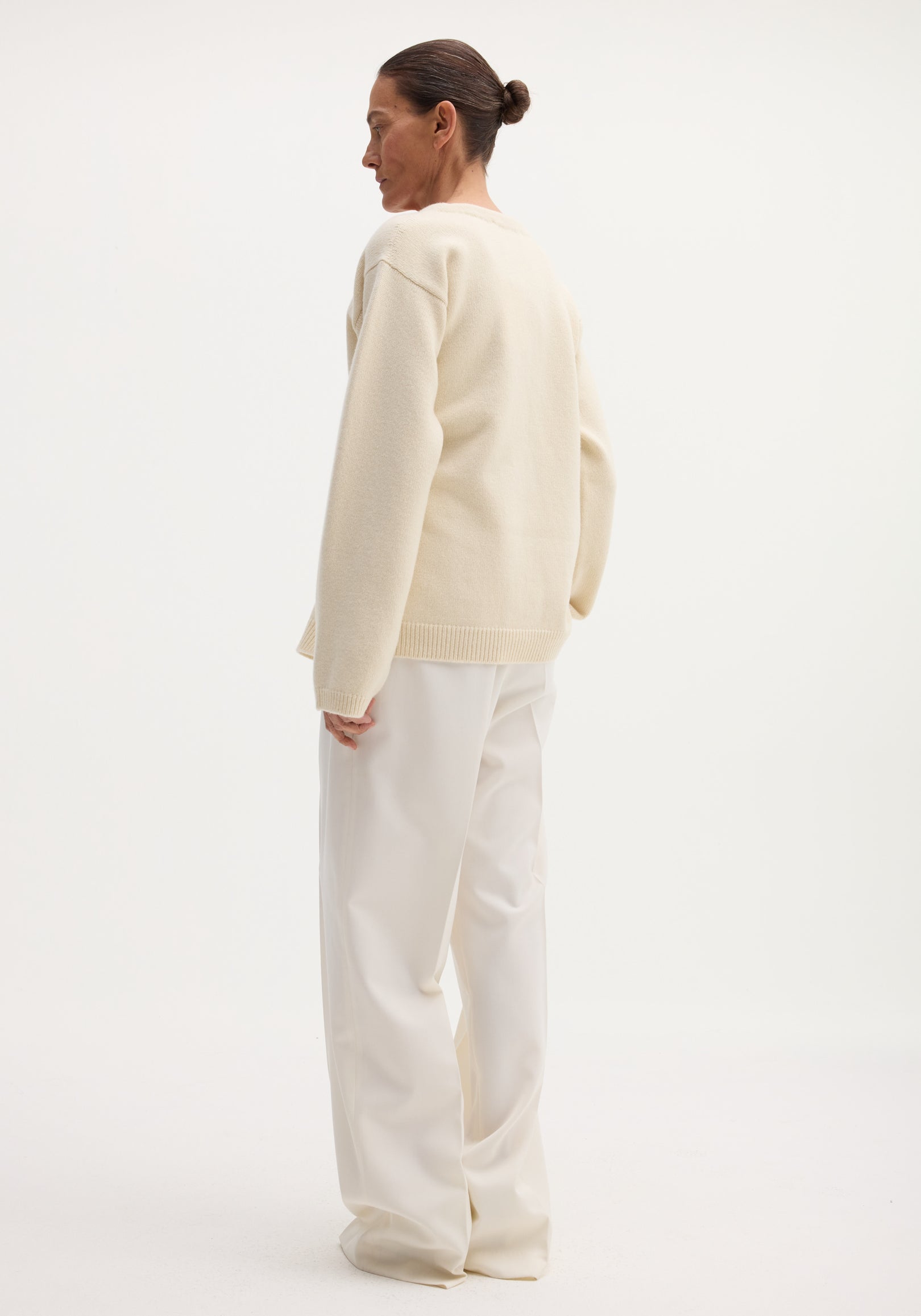 Person in profile wearing an Off-shoulder wrap cardigan | cream, showcasing its relaxed fit and safety-pin closure, paired with wide-leg trousers.