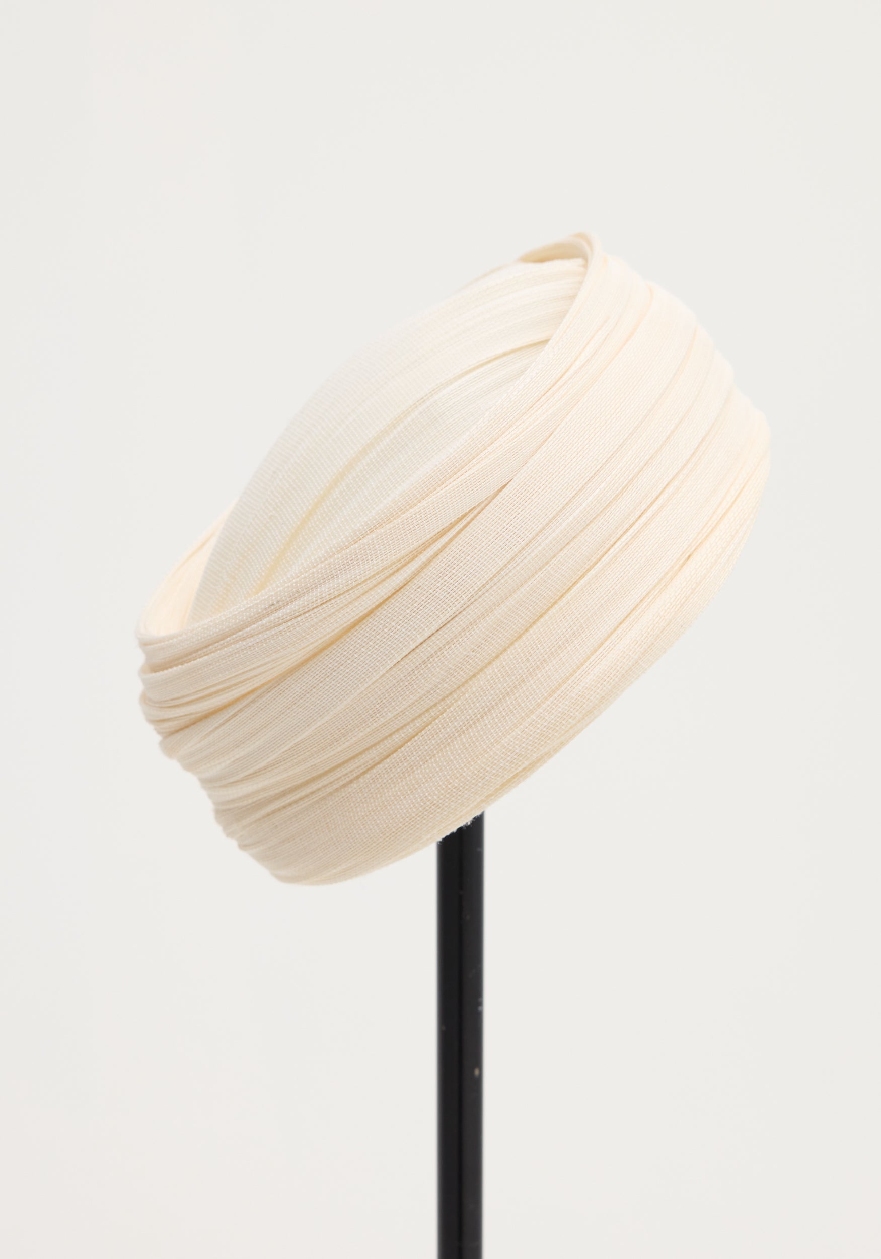 Sculptural silk hat | ivory with a finely pleated design, elegantly structured and displayed on a minimalist stand against a neutral background.
