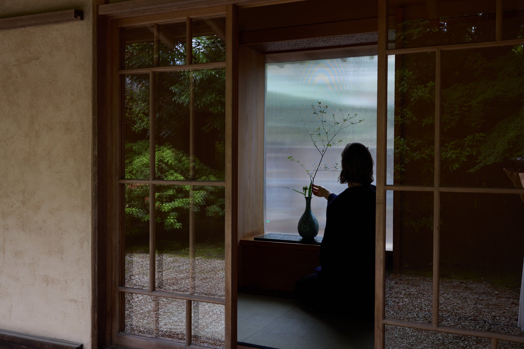 Woman sitting kneeled down in a Japanese tea house adjusting a branch in a vase 