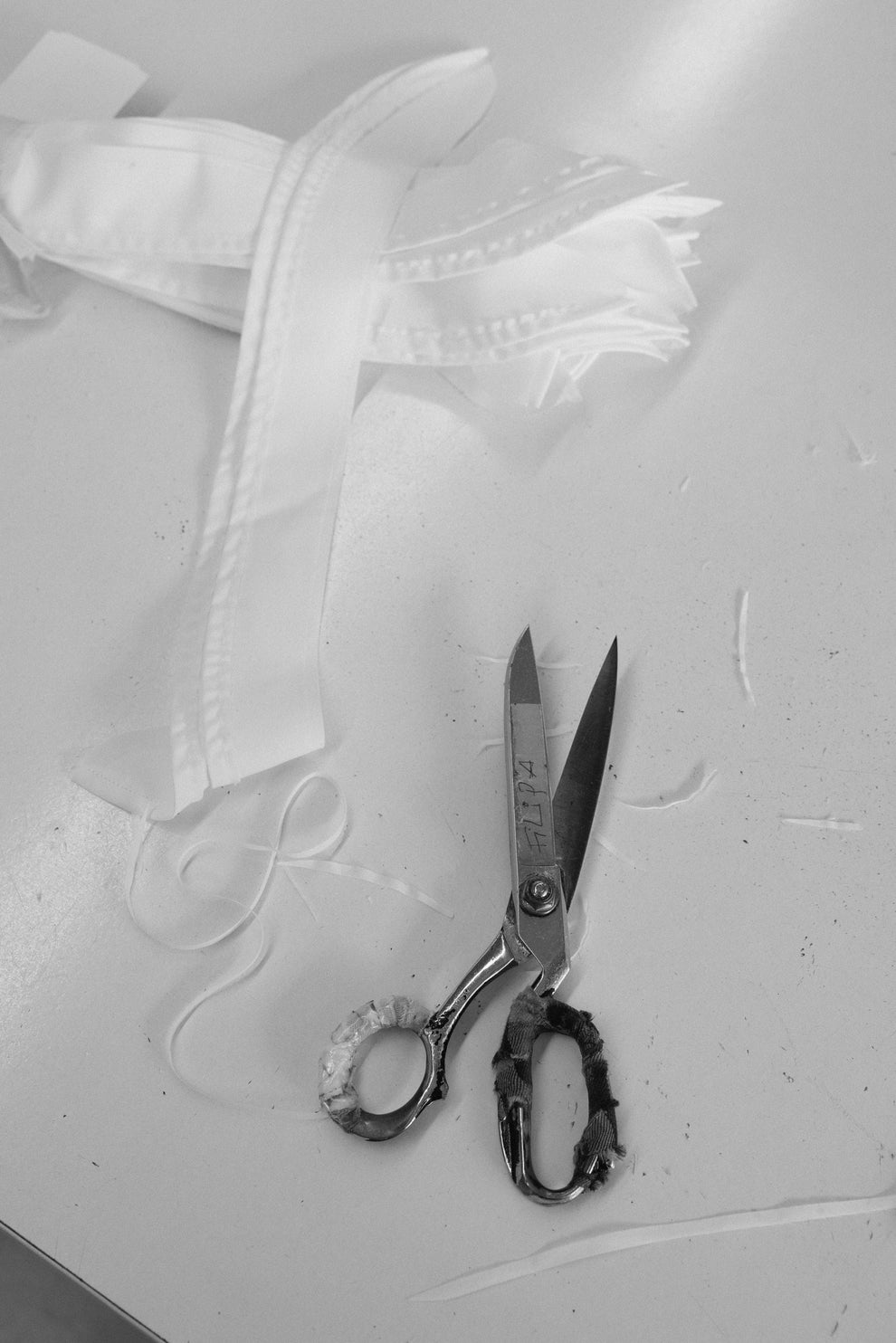 Scissors and a white cotton pieces of a shirt on a textured gray surface