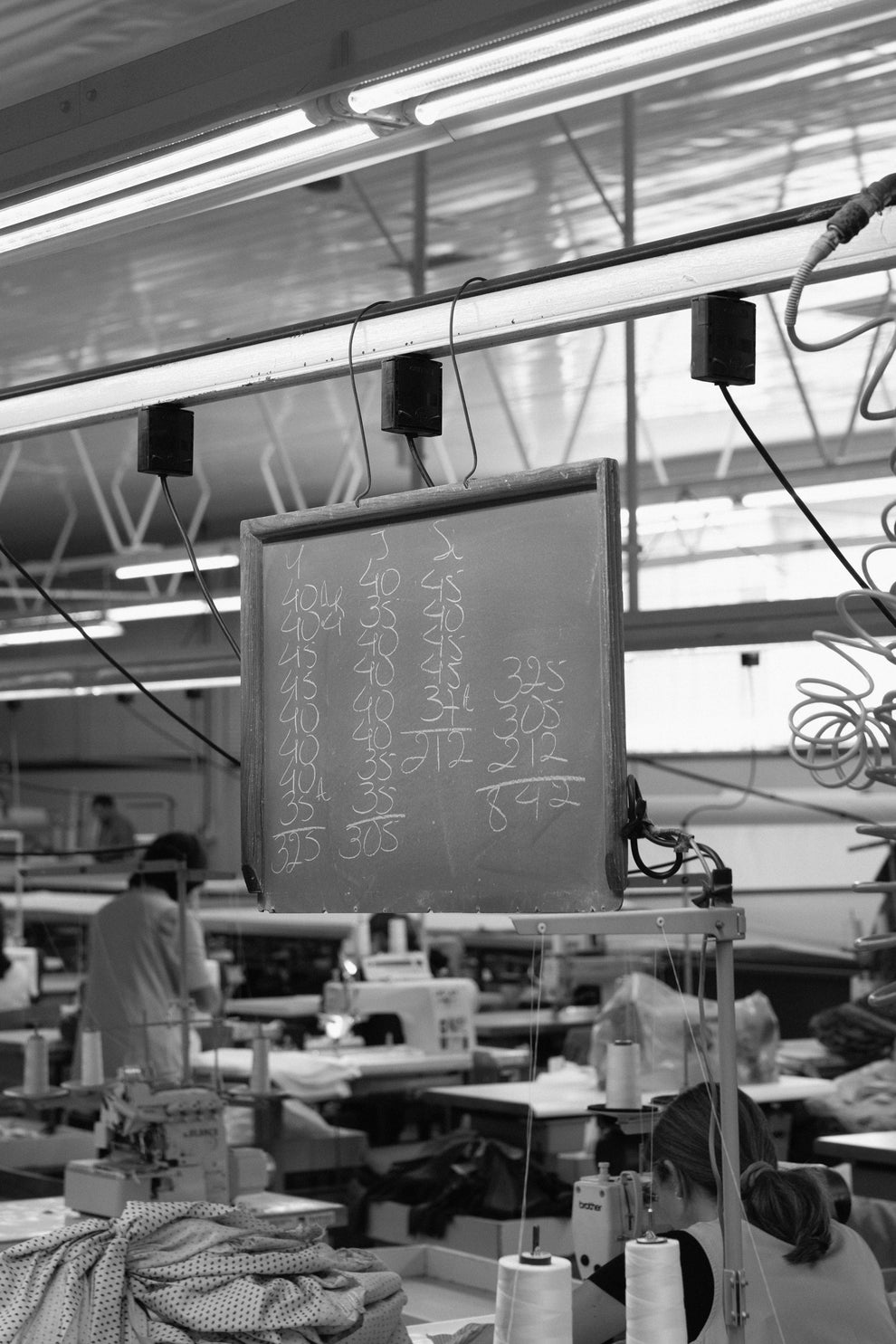 Factory interior with people and machinery, featuring a chalk board displaying numbers. 