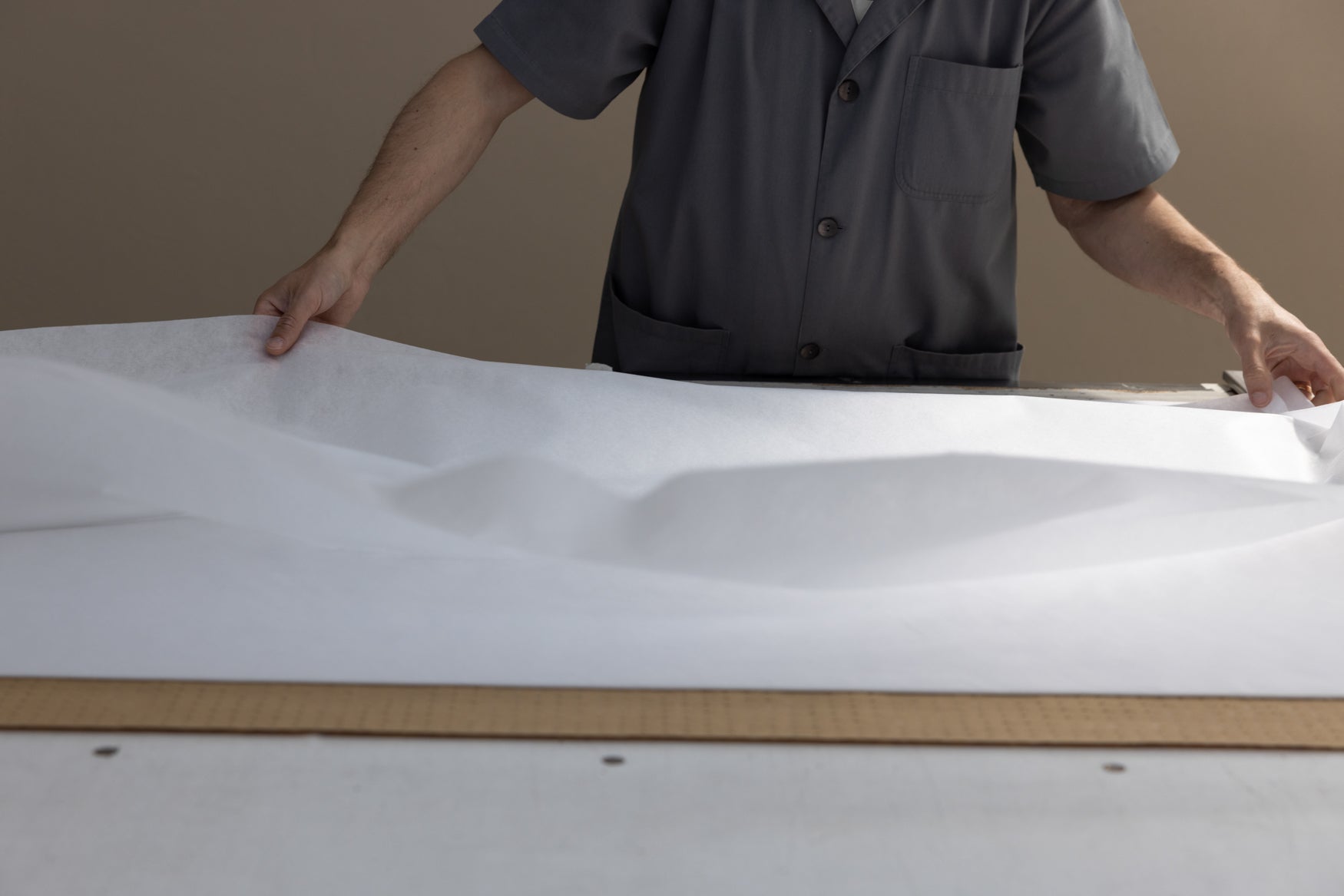 Person handling a large white sheet of paper or fabric on a flat surface.