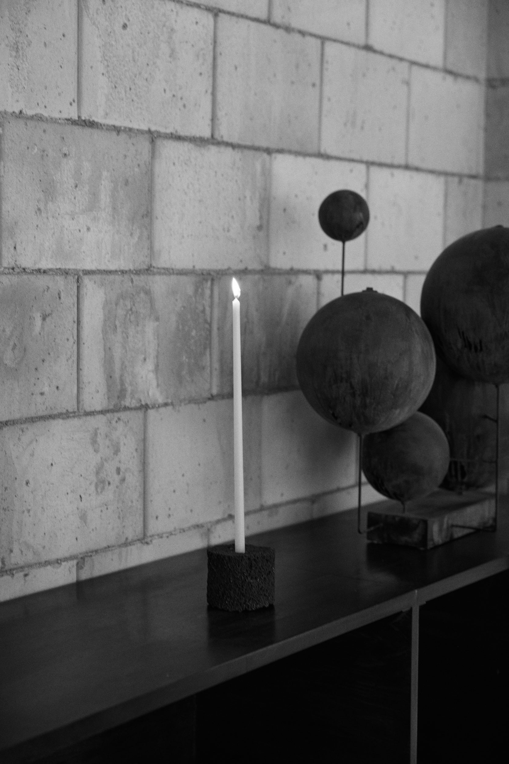 Candle on a stand with decorative spheres against a brick wall