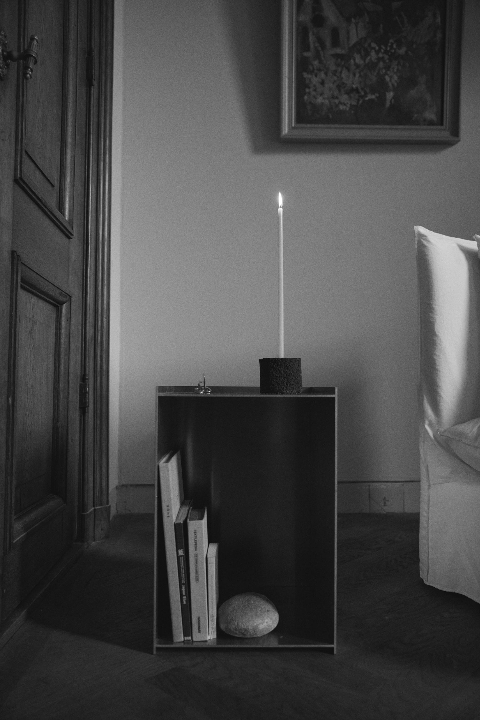 Round Candle Holder crafted from lava stone, holding a lit candle atop a cube side table with books and a stone, set in a serene interior.