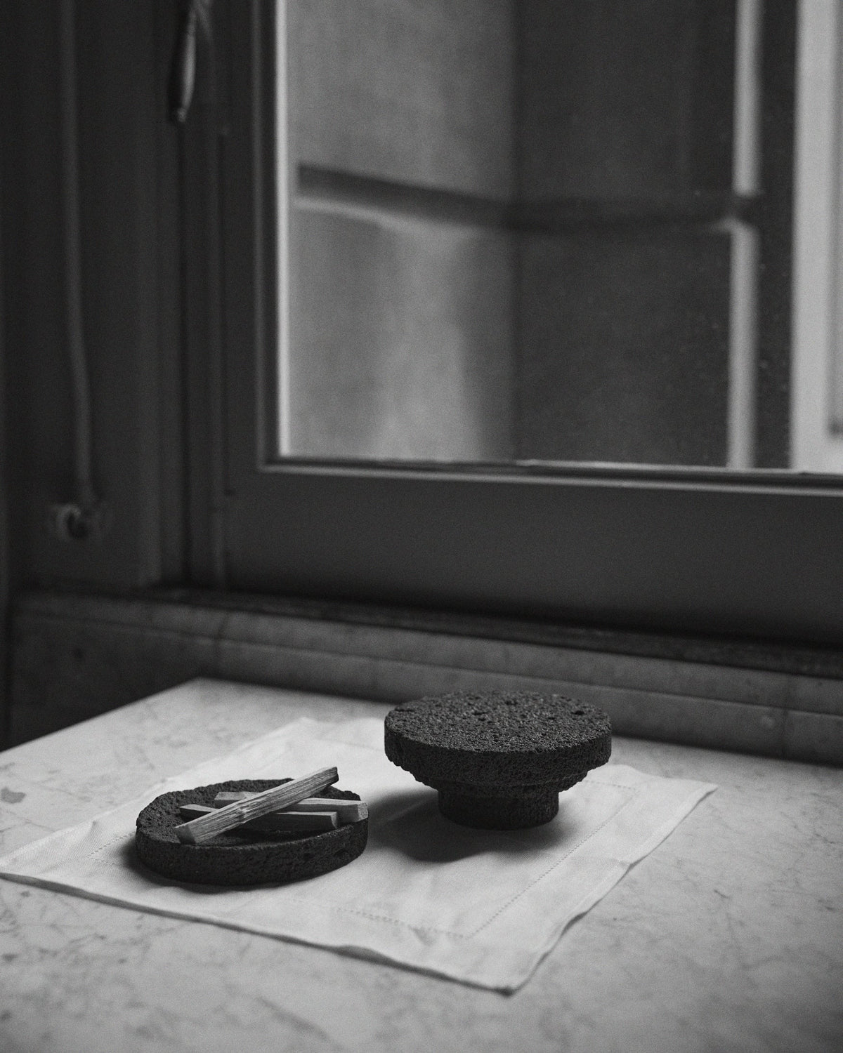 Elevated Sculptural Tray: Handcrafted lava stone tray with a shallow bowl holding slender wooden sticks, set on an inverted stone pedestal.